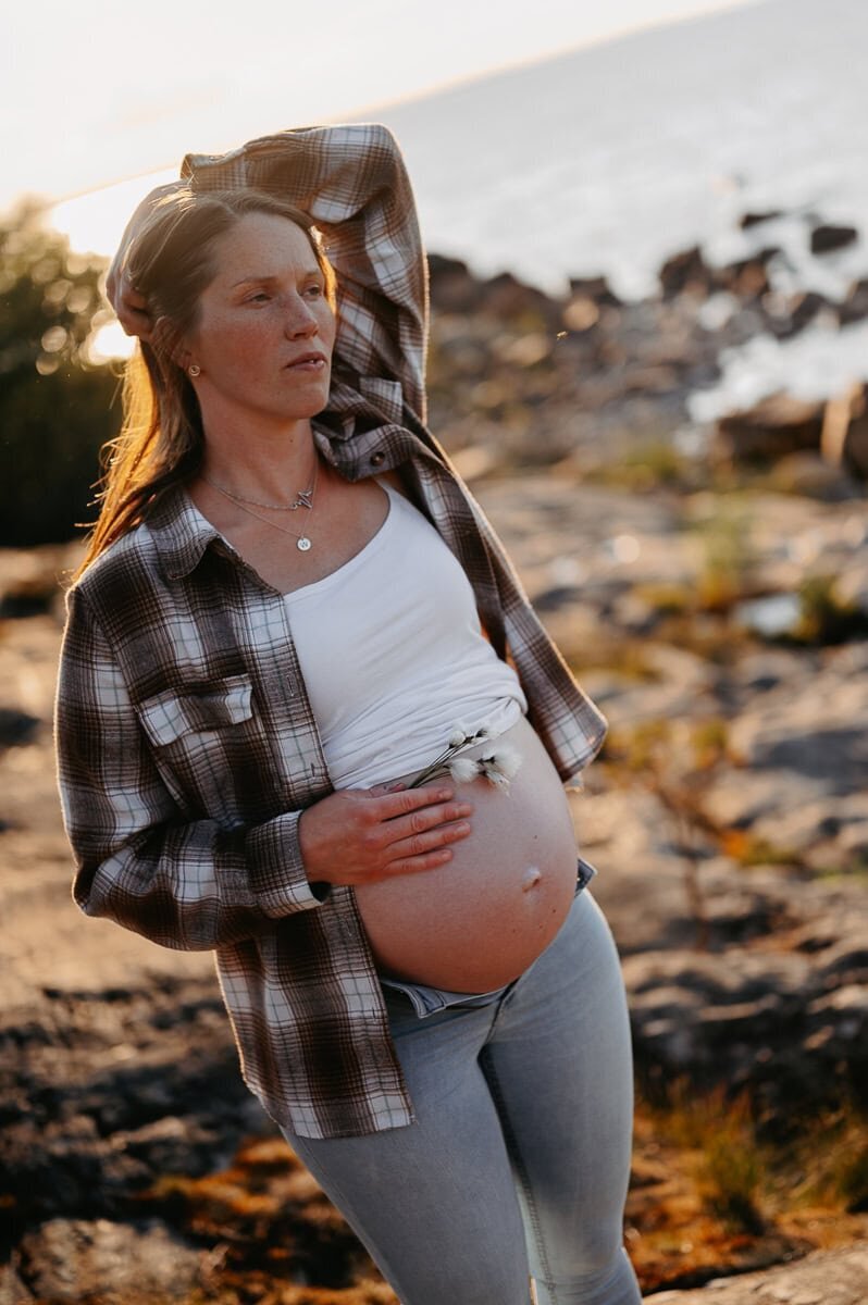 Gravid mamma har rutig skjorta som är öppen med blottande mage i solnegång.