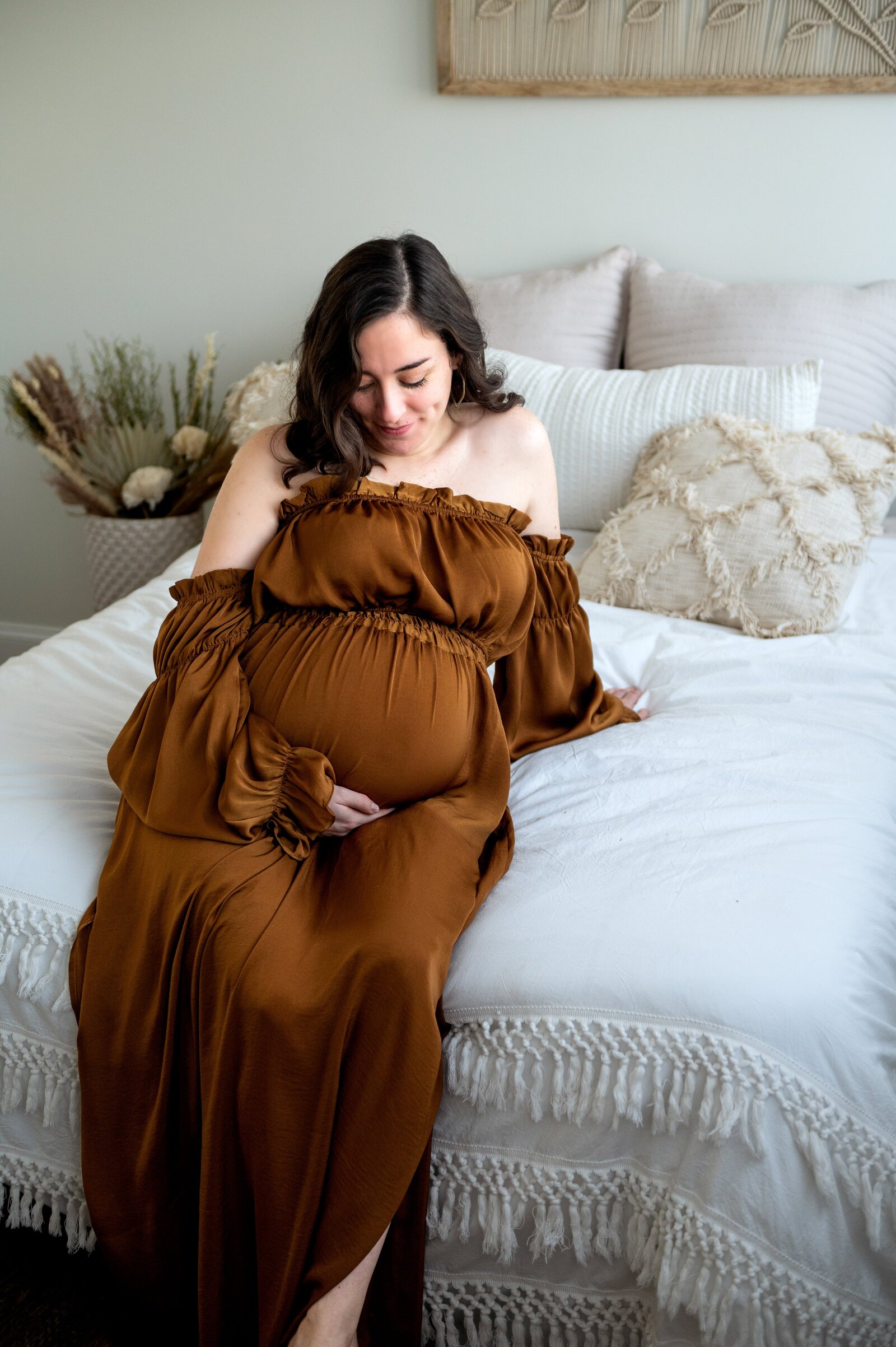 woman in a brown dress on a bed holding her belly