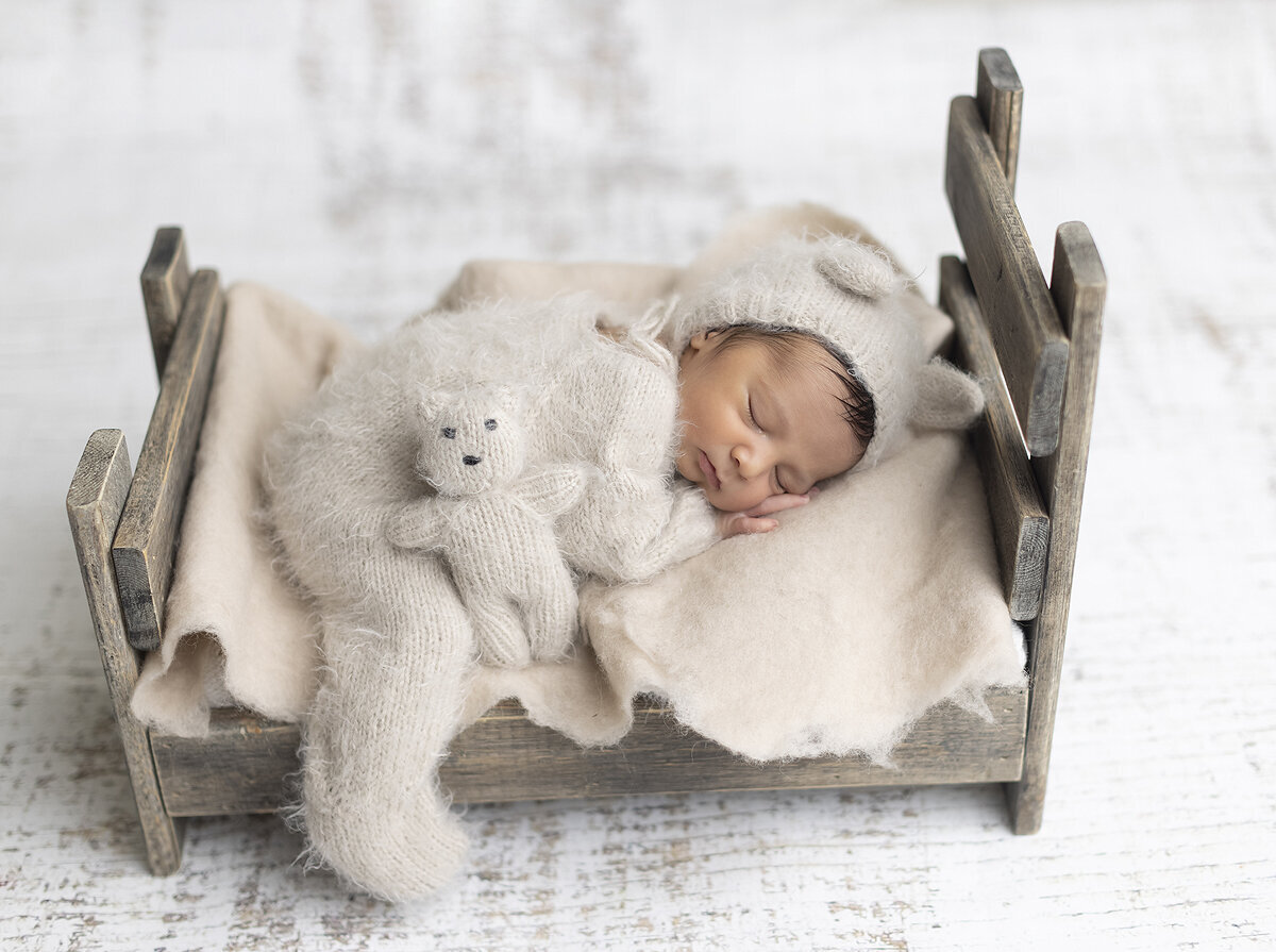 Newborn boy in teddy bear outfit on a small bed.