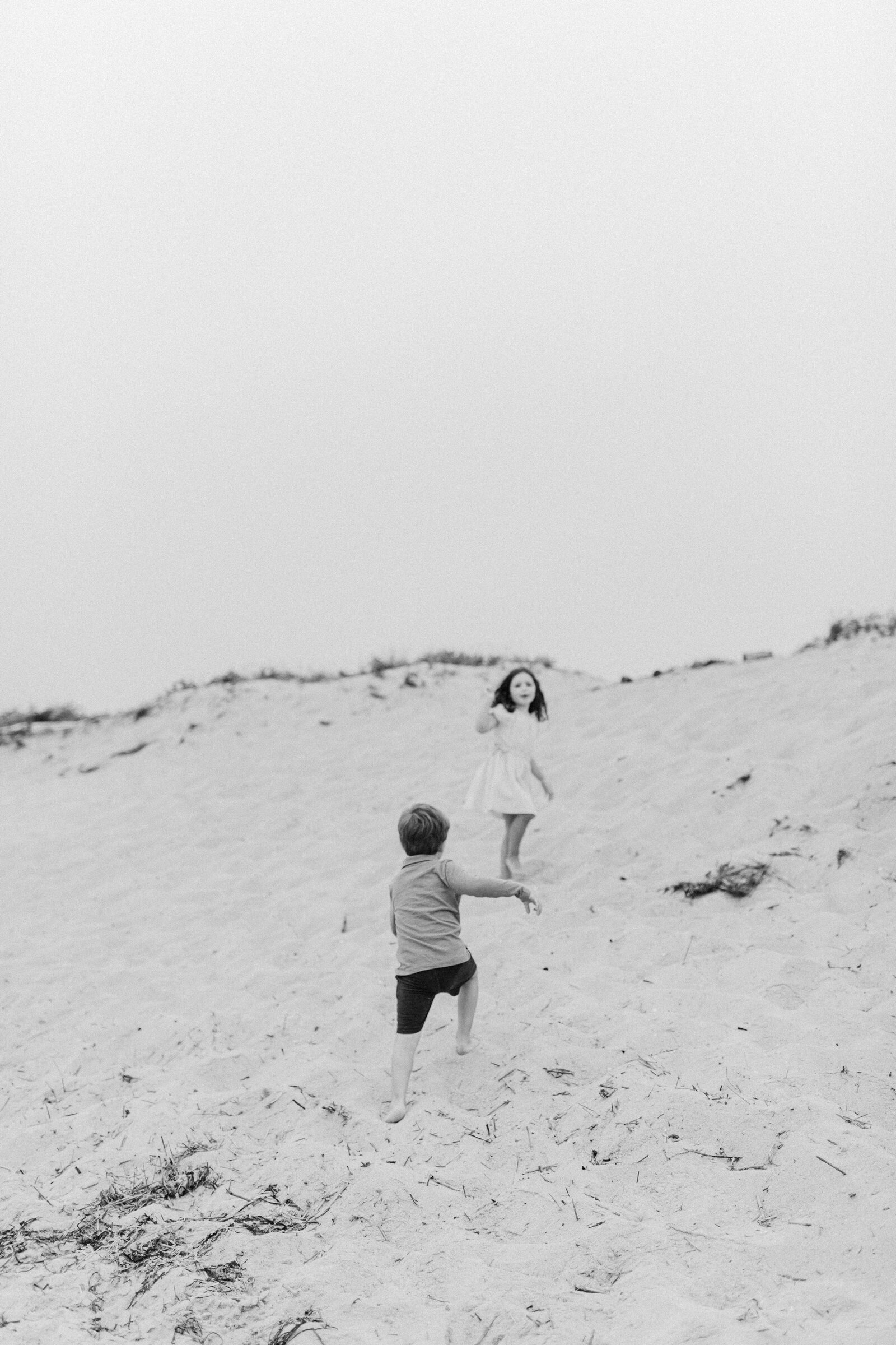 A black and white image of a young boy and girl climbing up a hill at the beach
