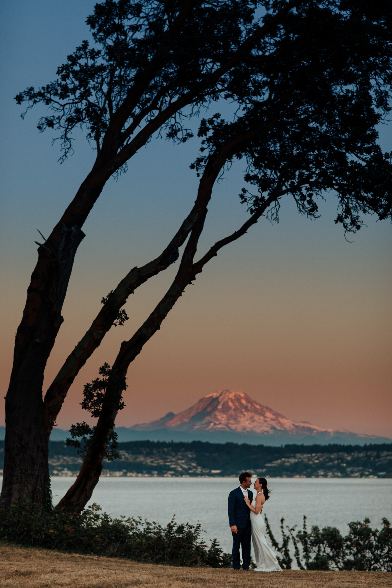 Bride and groom at Vashon waterfront  at sunset with Mount Rainier visible in the distant.