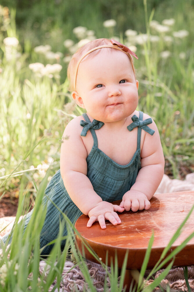 a baby girl in a green dress sits by a log in the woods
