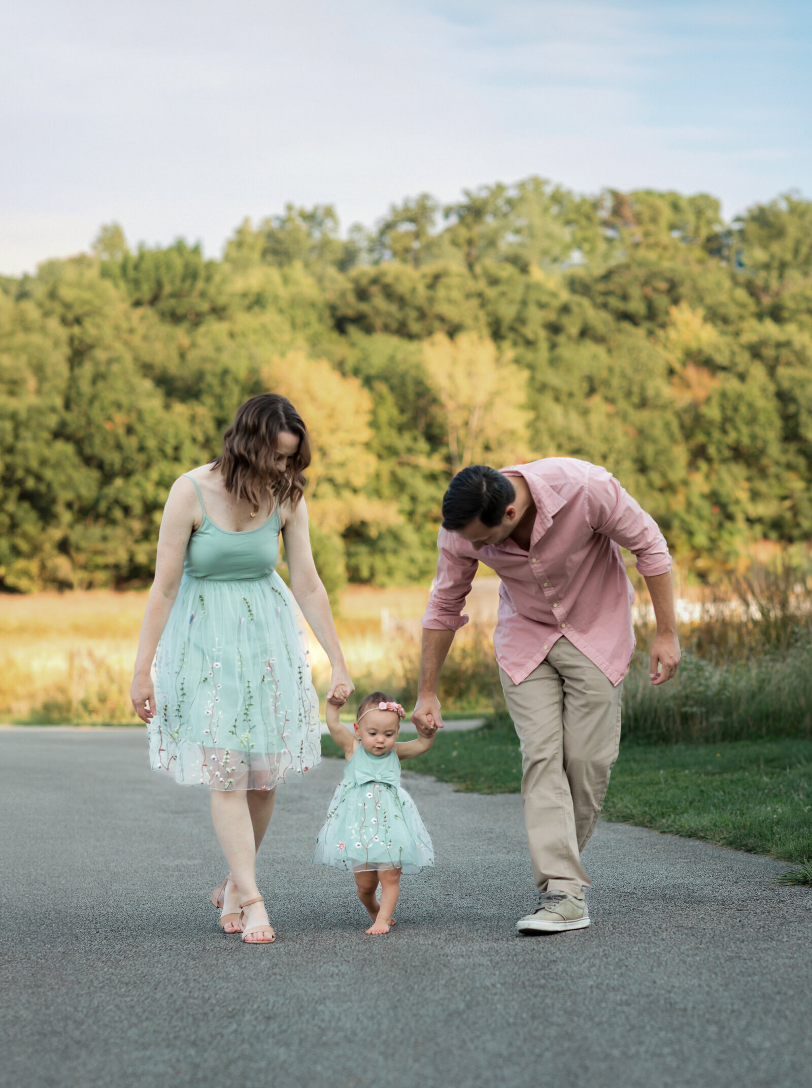mom and dad holding hands with daughter walking in park for family photos