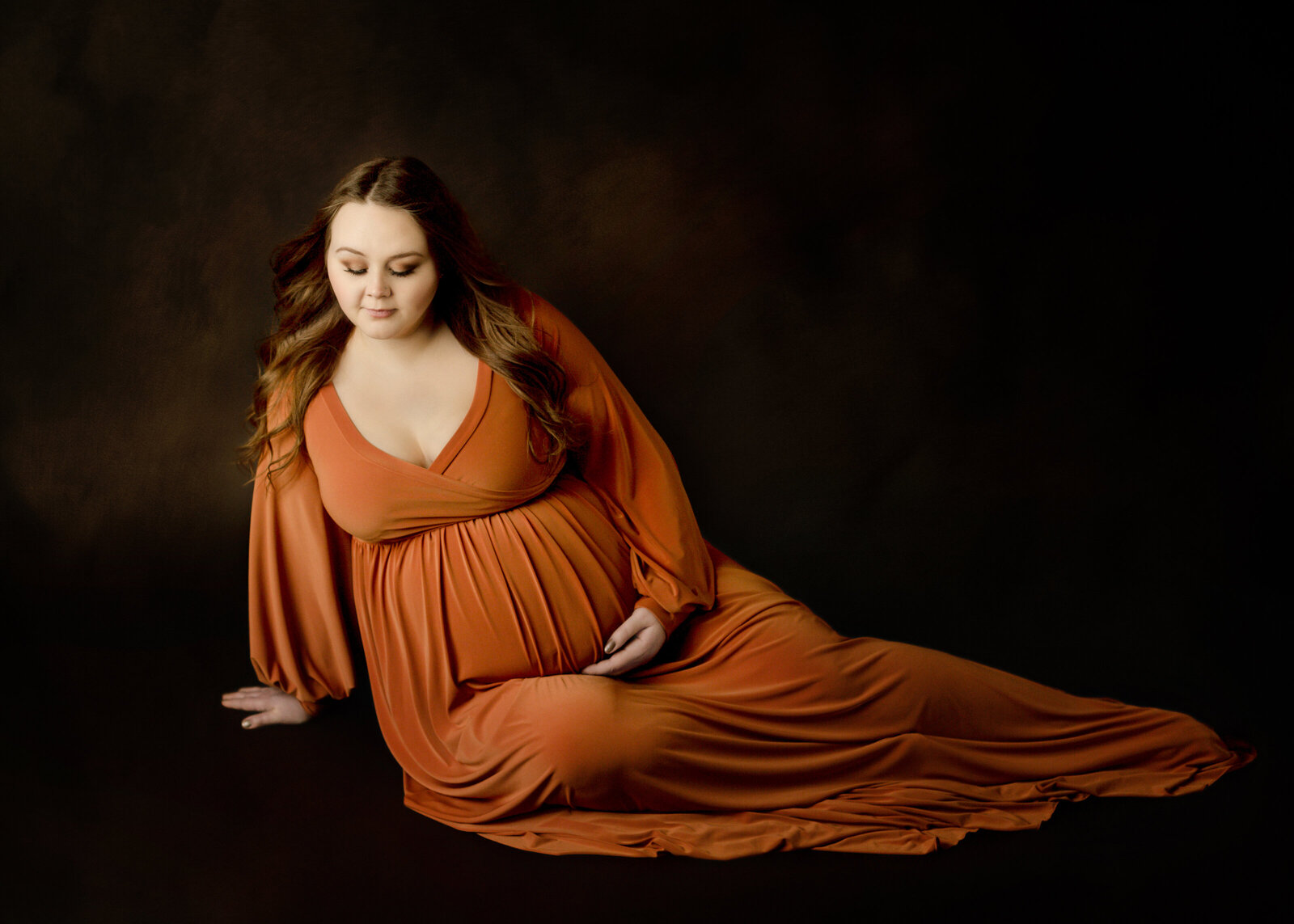 Pregnant woman sitting on the ground in a orange gown