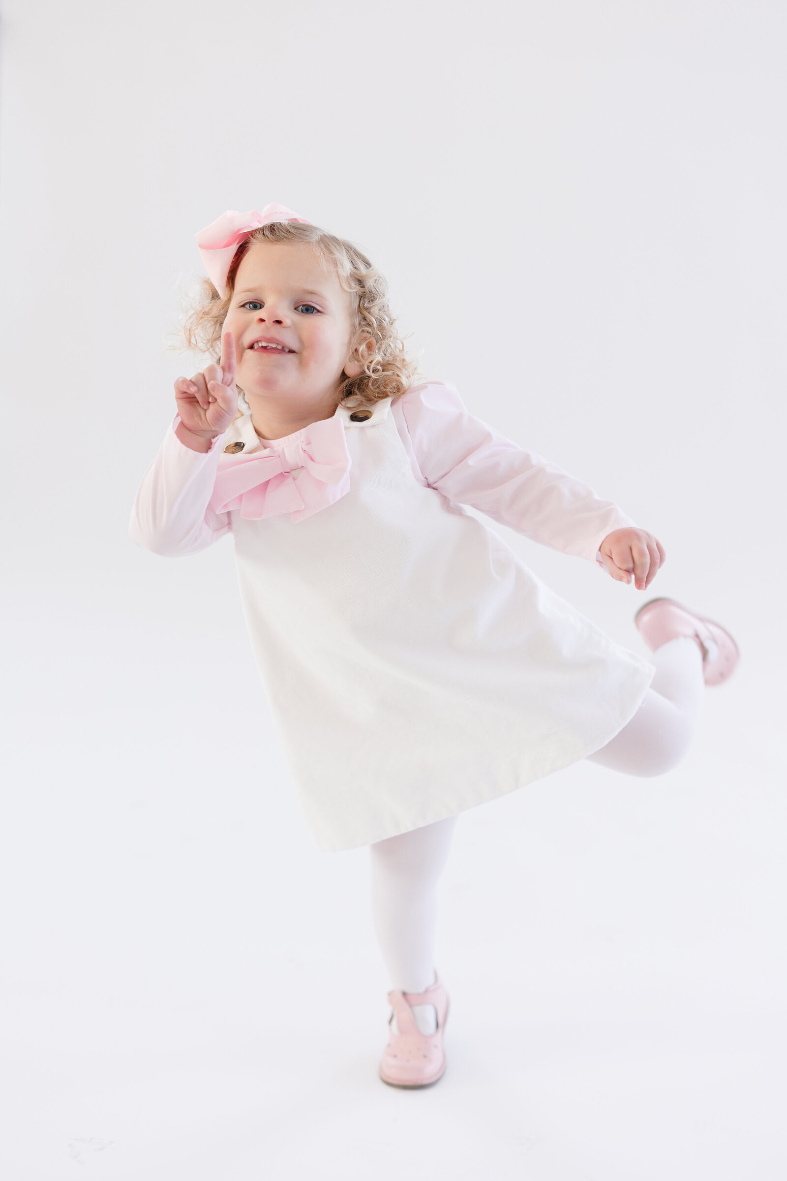 Little girl wearing a white and pink dress as she twirls and makes a silly face