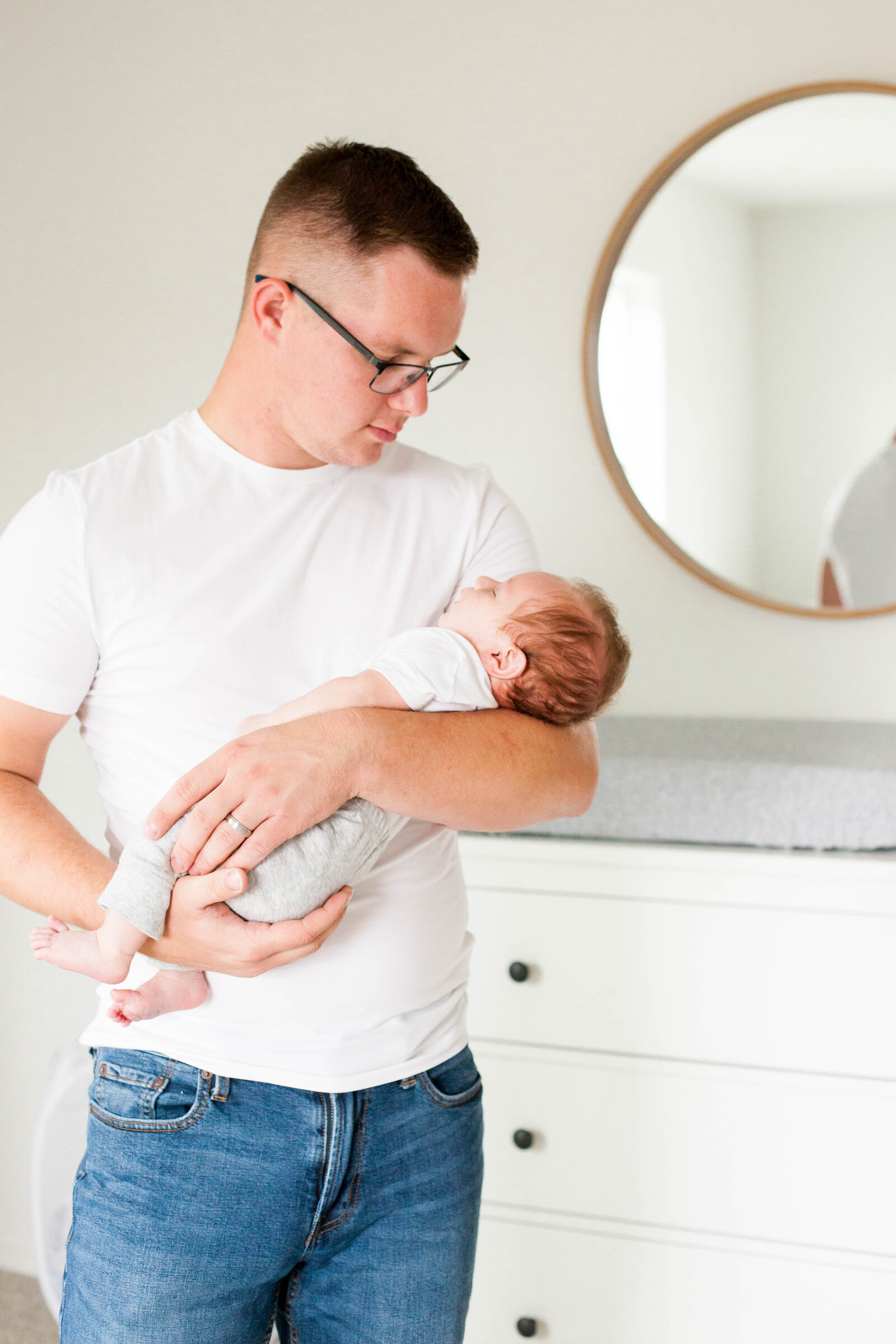 A father in a white tee shirt, holding his newborn baby.