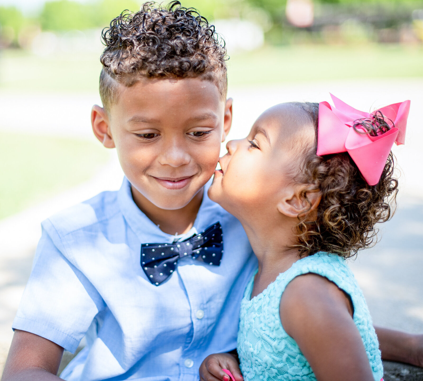 young boy wearing a bow tie receiving a kiss on the cheek from his sister photographed by Millz Photography in Greenville, SC