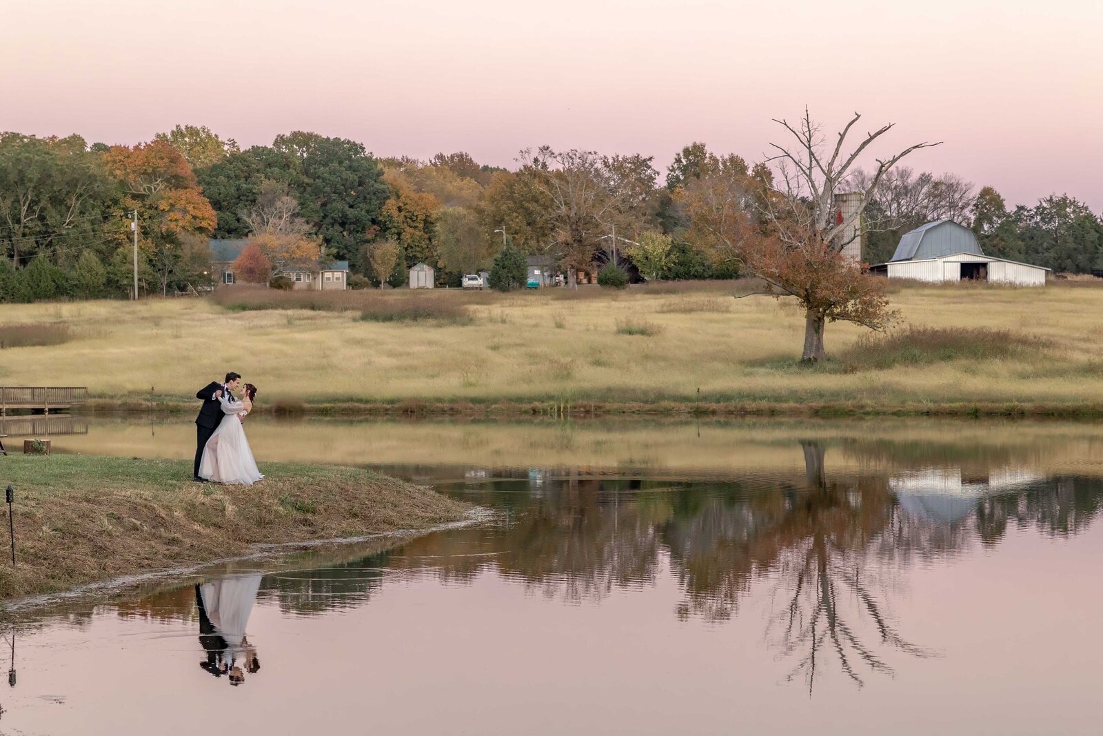 The bride and groom share a quiet moment by a reflective pond at sunset during a Boone, NC wedding, with a serene countryside backdrop and vibrant autumn colors.