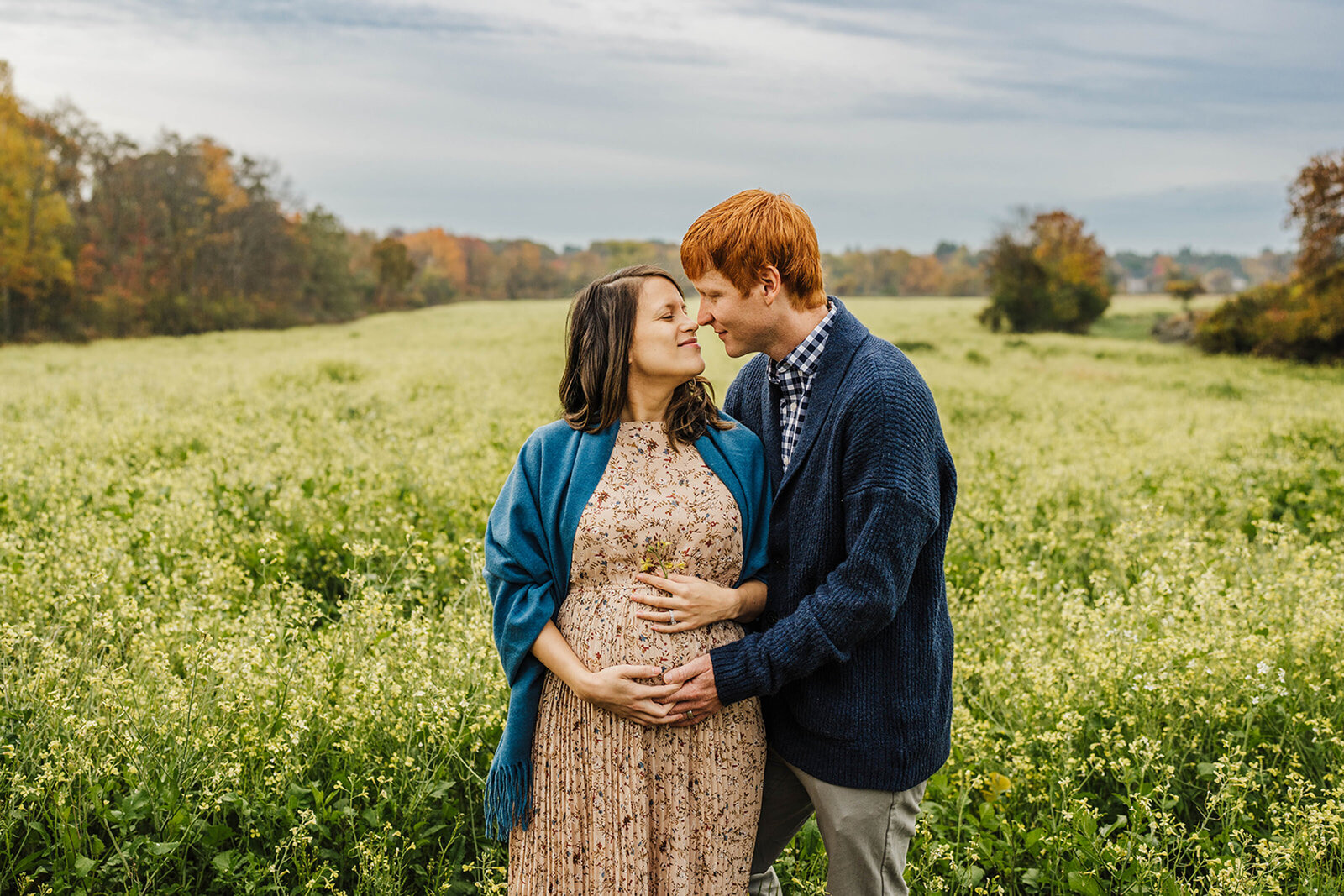 wide angle view of pregnant couple posing in field of yellow flowers