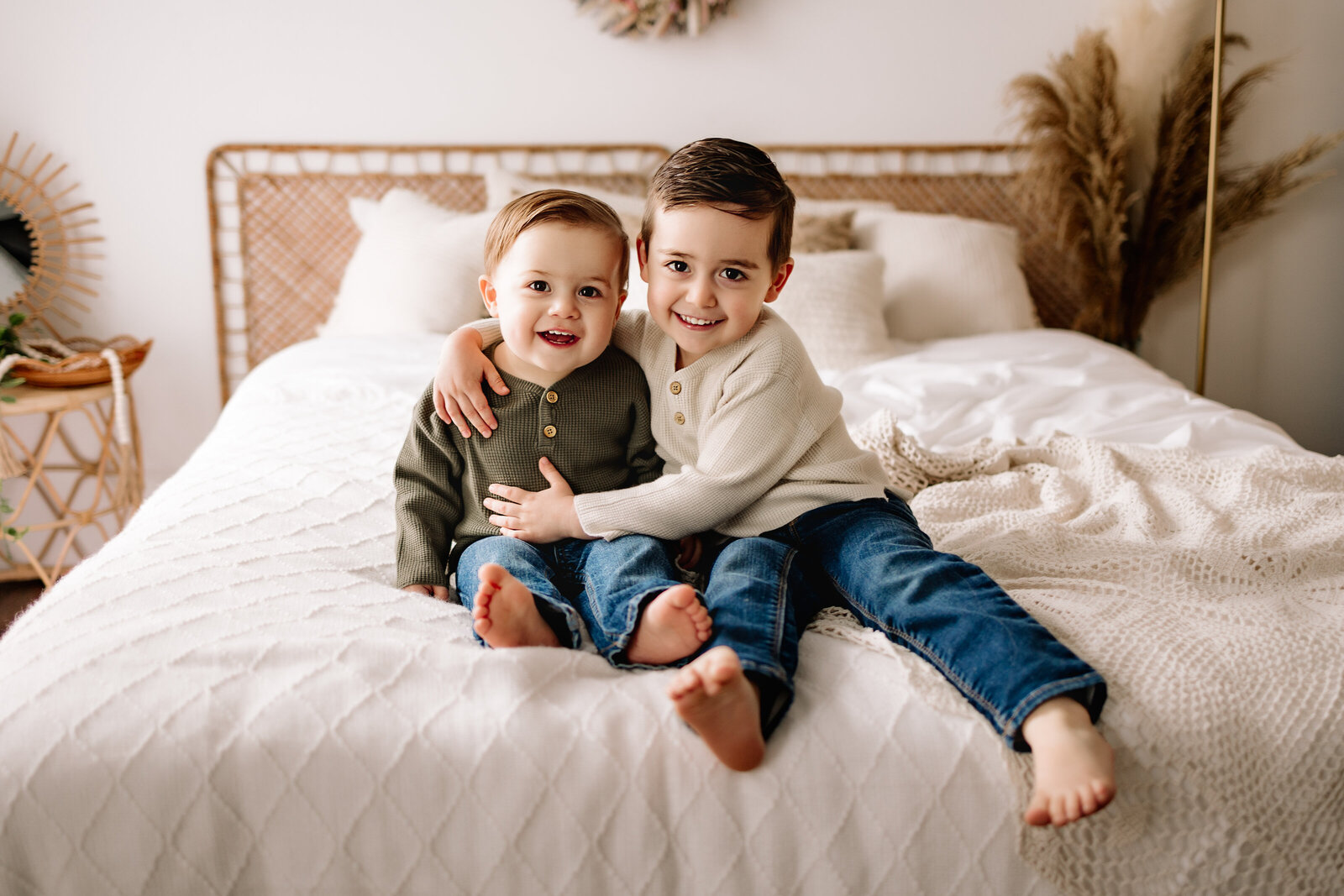 Two little boys snuggle up together on a bed with boho decor