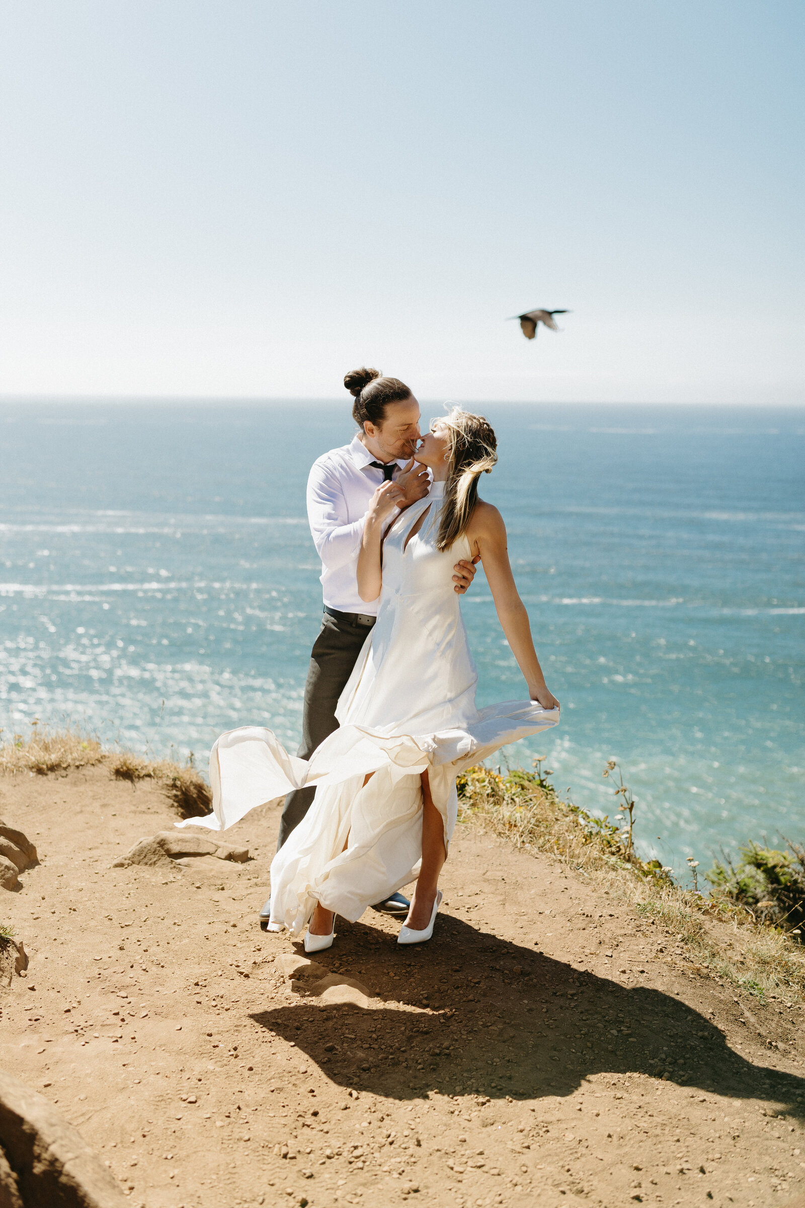 A couple snuggles in close for a bridal portrait on the end of a cliff overlooking the ocean.l