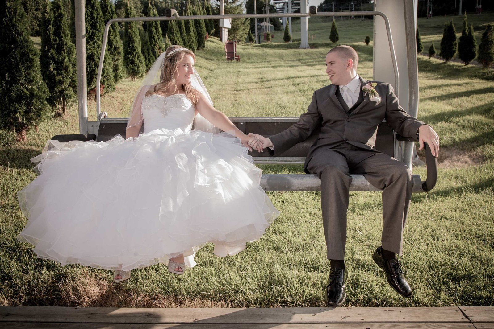 Bride and groom hold hands on ski lift in California.
