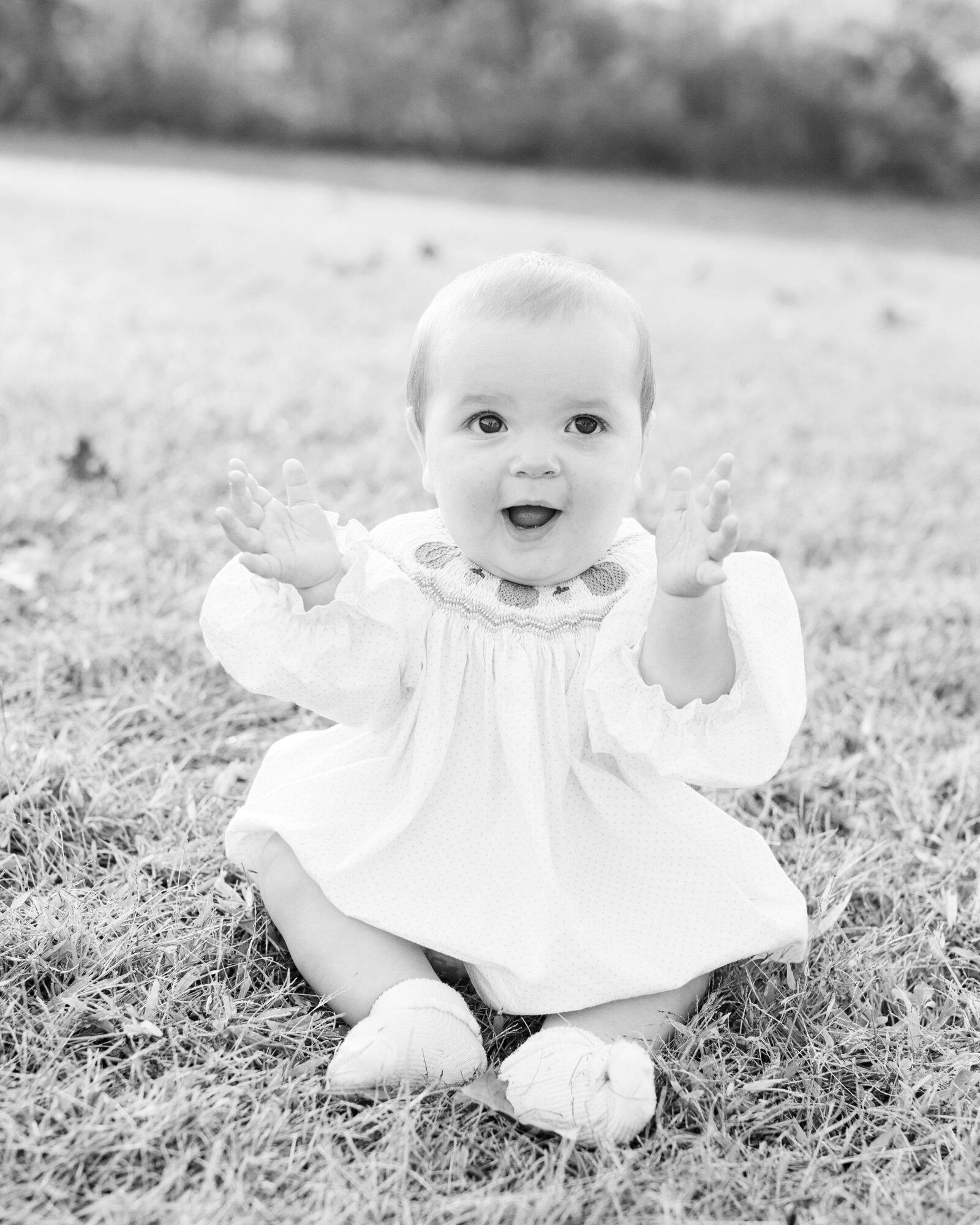 A black and white portrait of the youngest Taunton daughter smiling in a smocked dress, captured by Abby Bell Photography, Fine Art Portrait Photographer based in Alabama.
