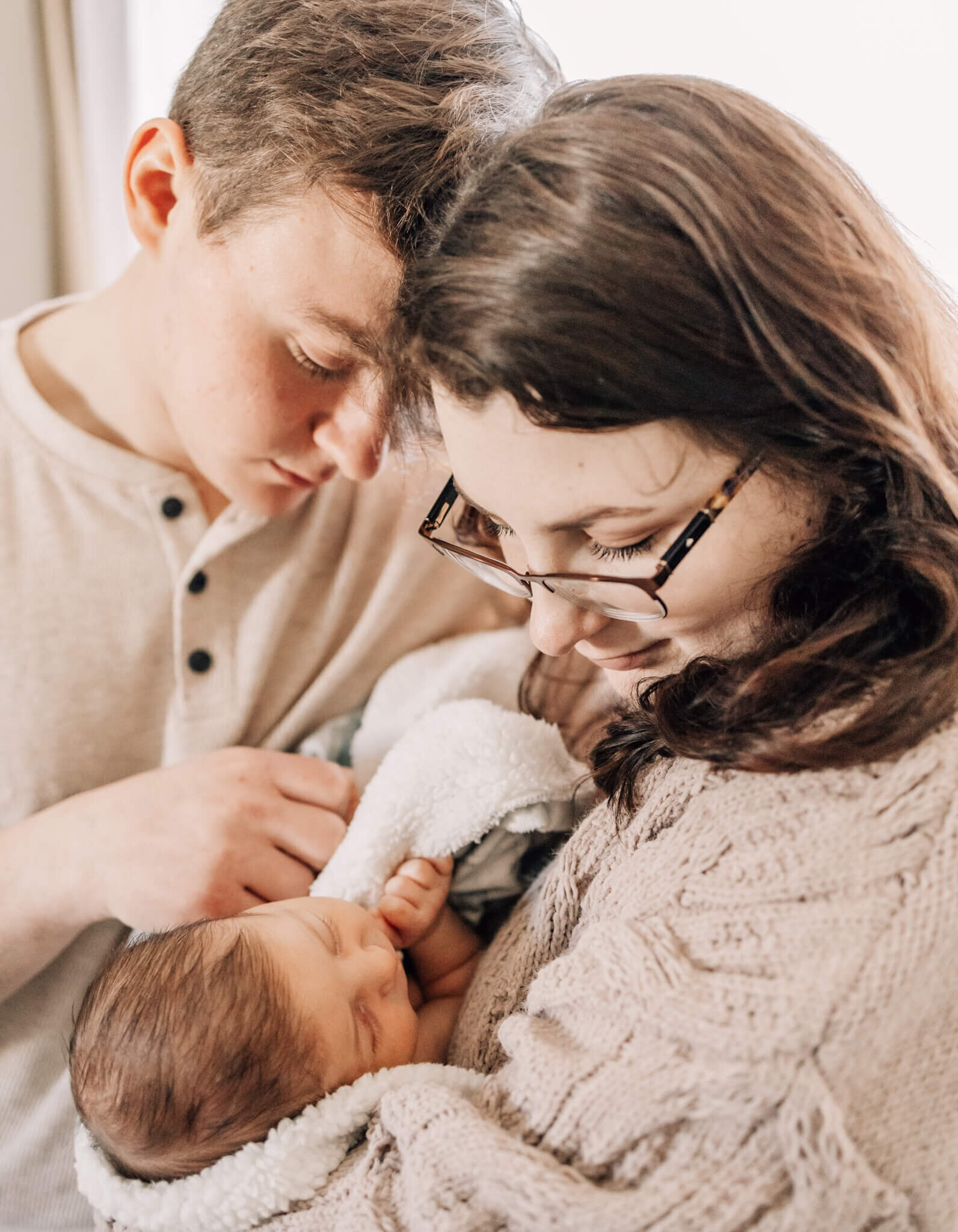 Mom and dad looking down and snuggling baby.