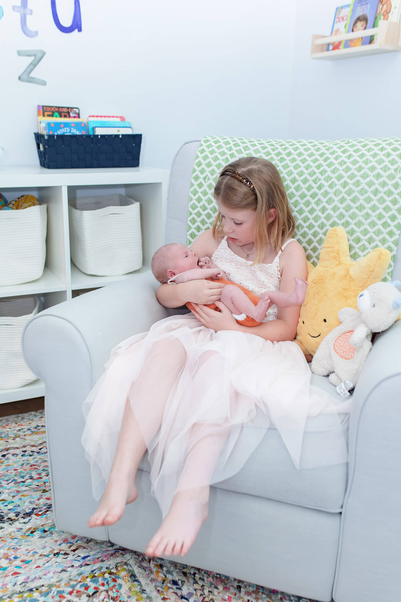 A little girl holding her newborn brother in a chair.