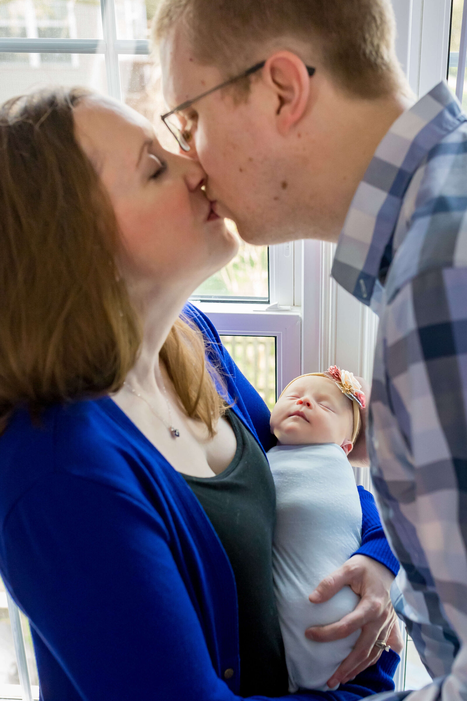 A Manassas couple snuggling their newborn girl and kissing.
