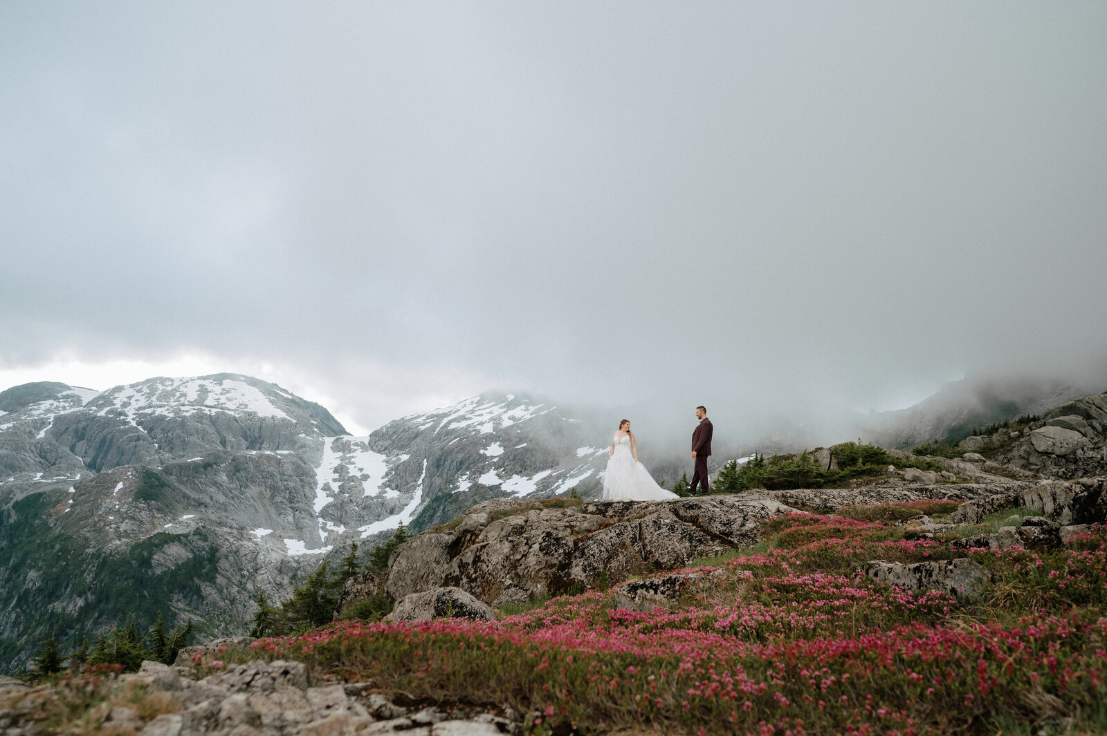Helicopter elopement package in British Columbia with bride and groom on a snowy mountain ridge