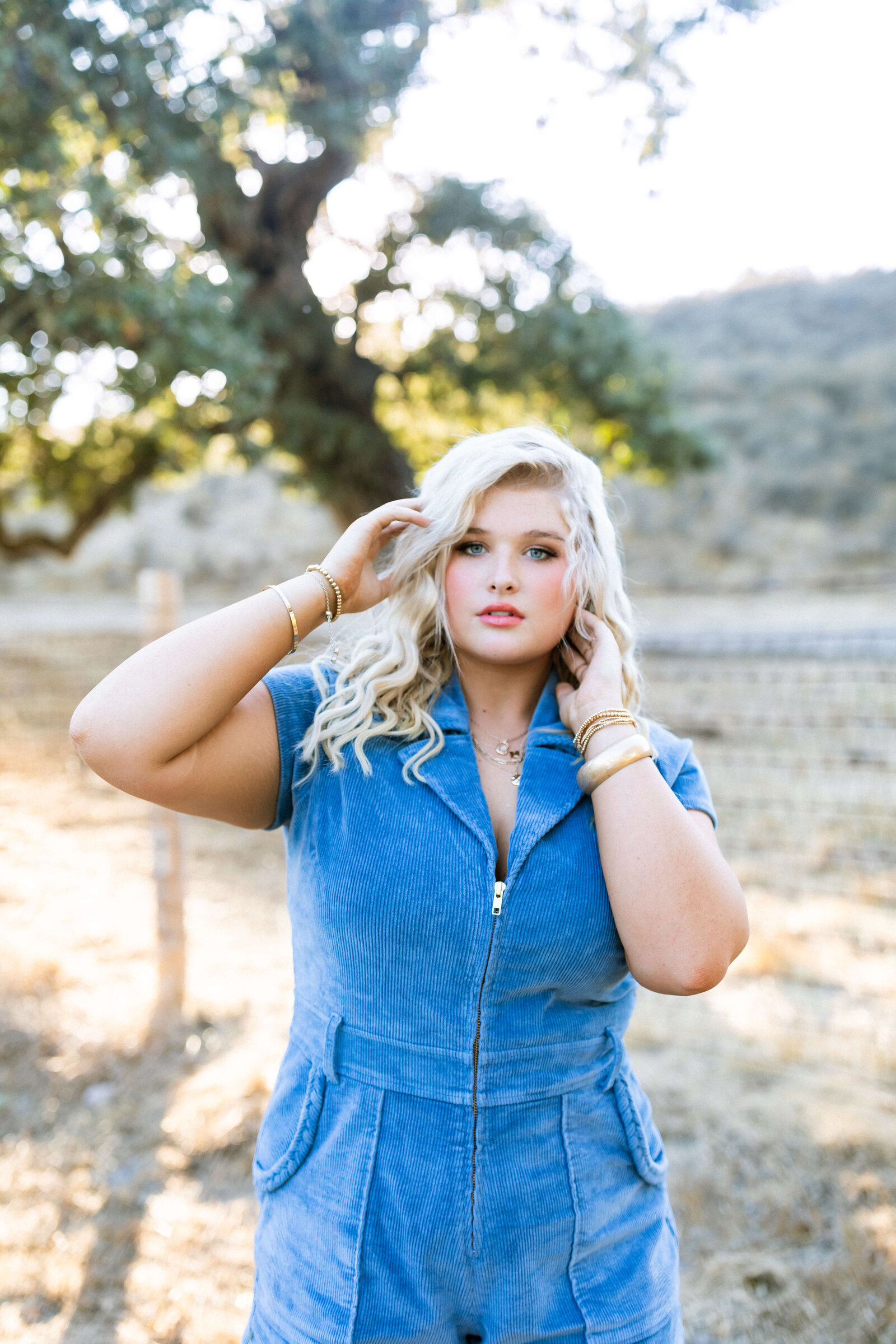 blonde girl wearing blue jean romper posing in a ranch