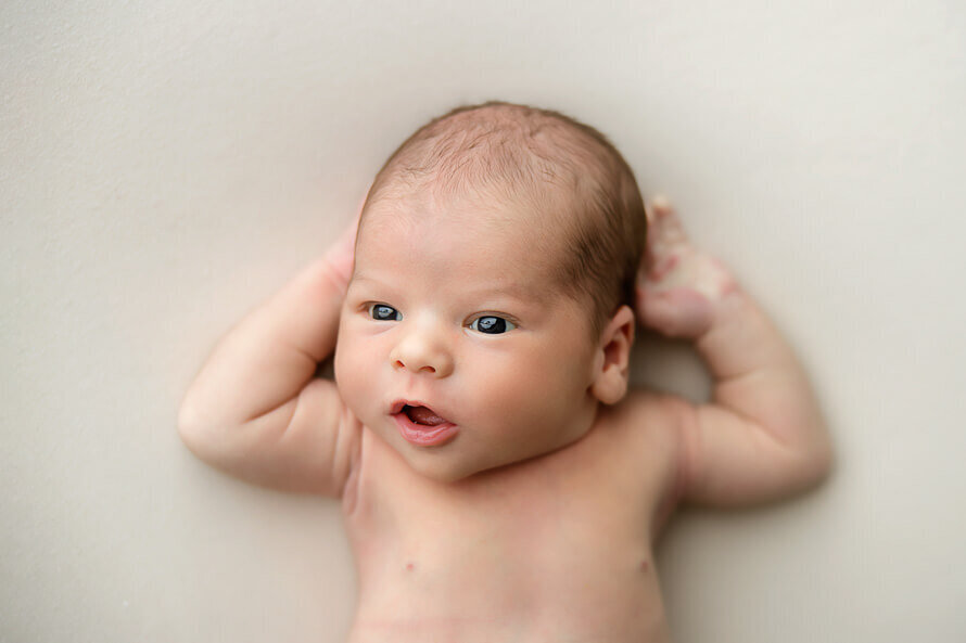 Awake baby has hands behind head.