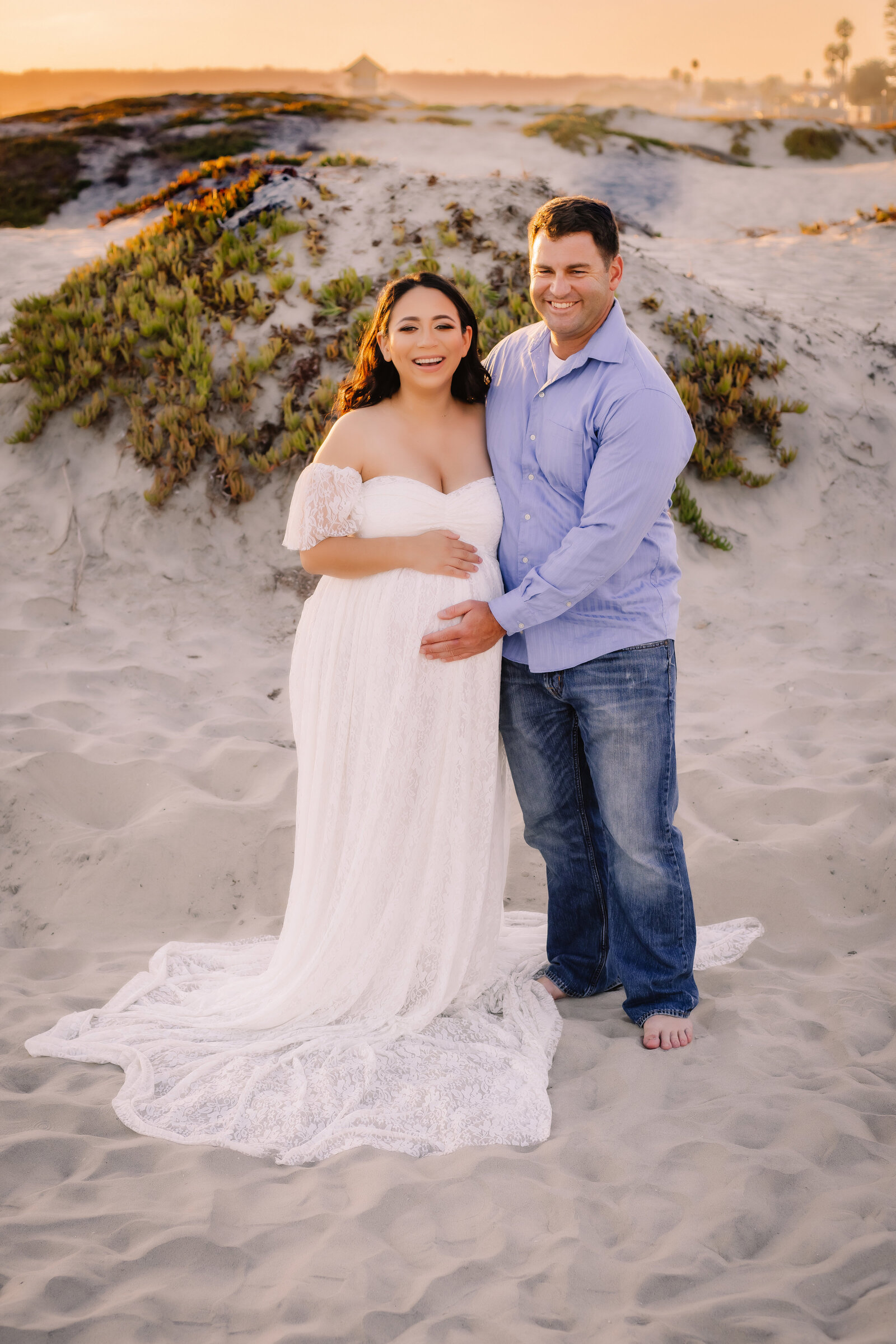 Maternity Photographer, a man and woman hold each other in the sand, she is expecting