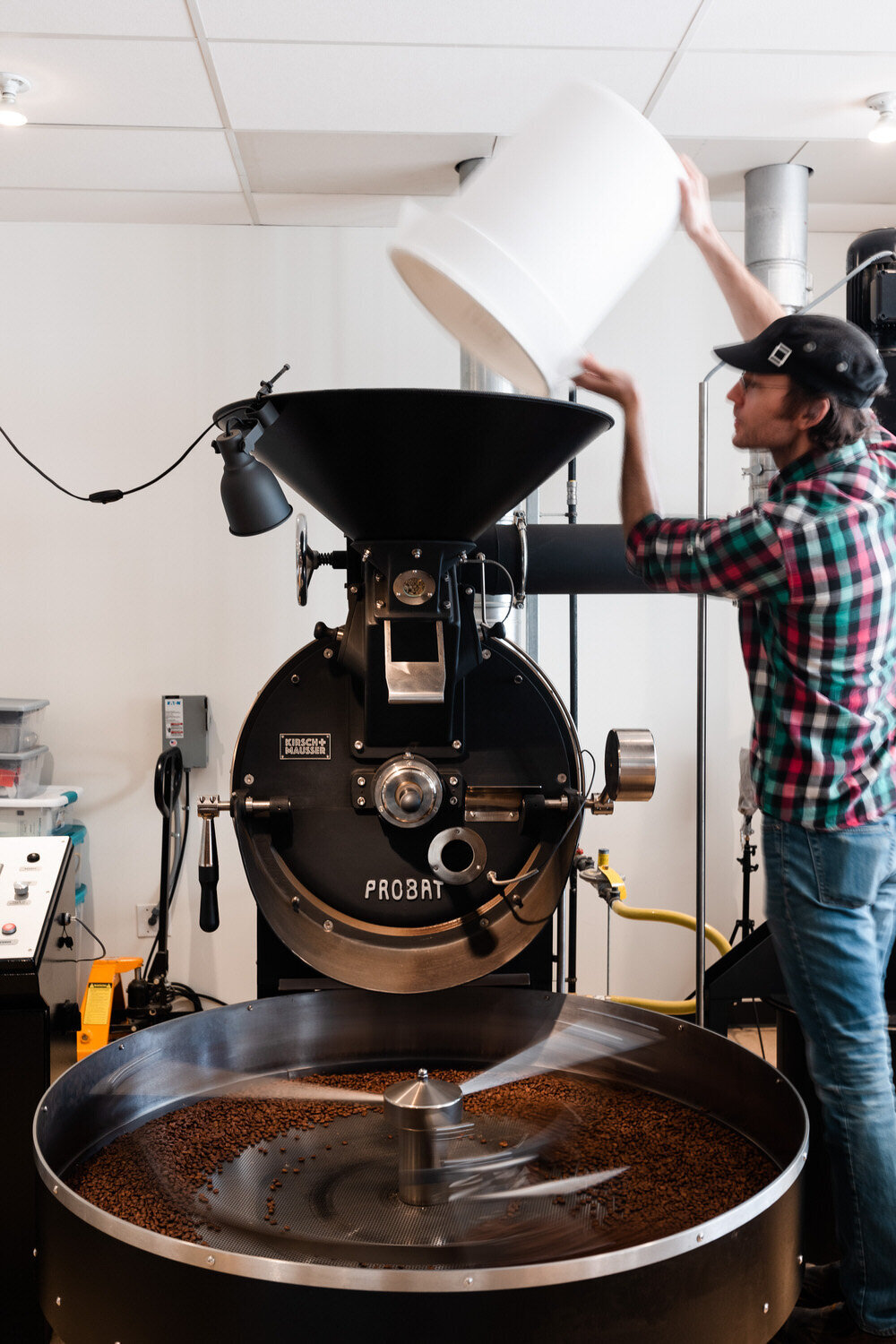 man pouring a bucket of coffee beans into a large machine
