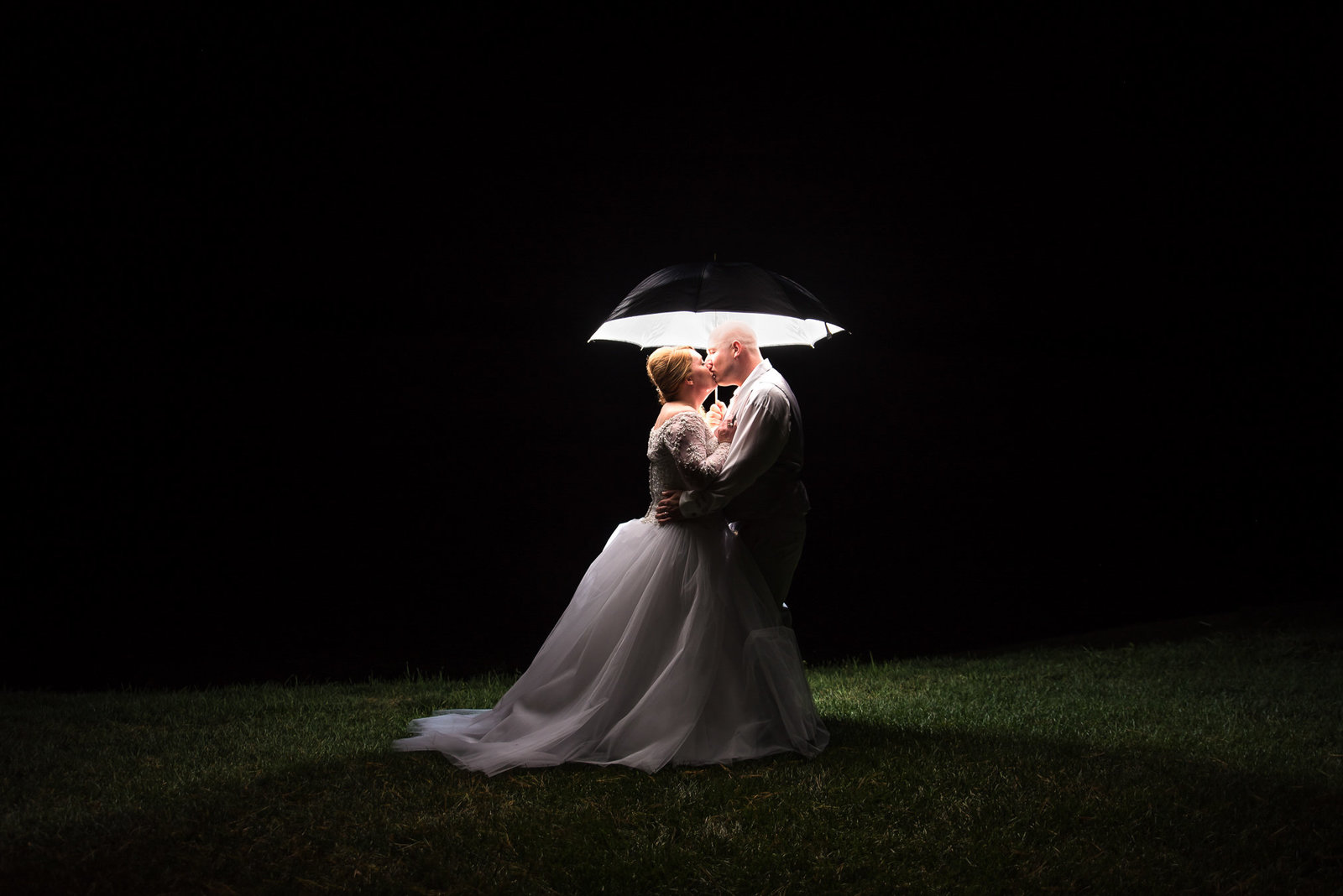 Bride and groom pose for a nightime picture under a lit umbrella