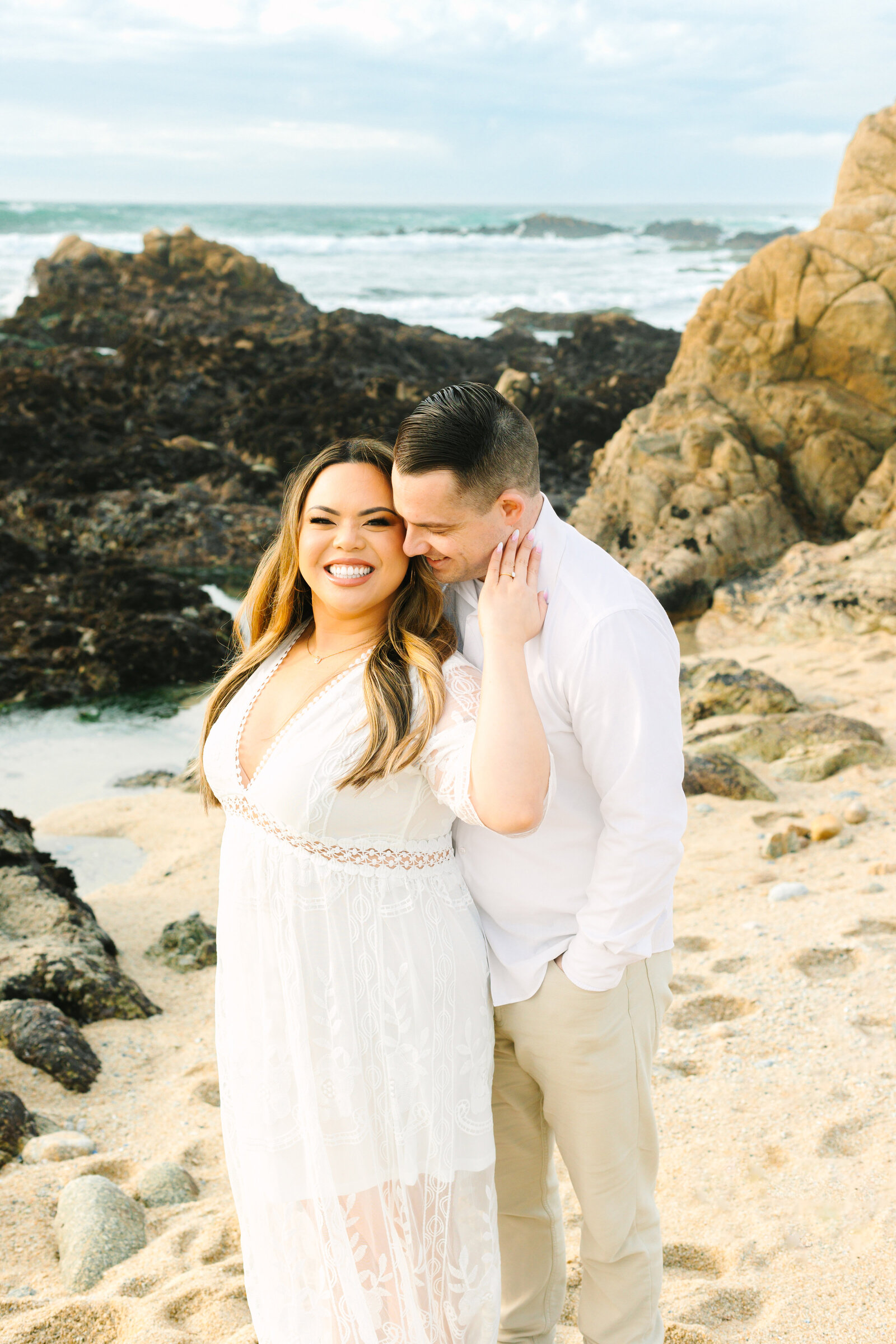 An engaged man and woman take photos on the beach in Pacific Grove, Monterey, California near Big Sur.