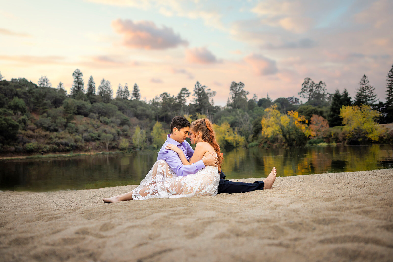 Engaged couple sit on the beach in front of a lake and press their foreheads together smiling. Photo by wedding photographer studio in Sacramento, Philippe Studio Pro.
