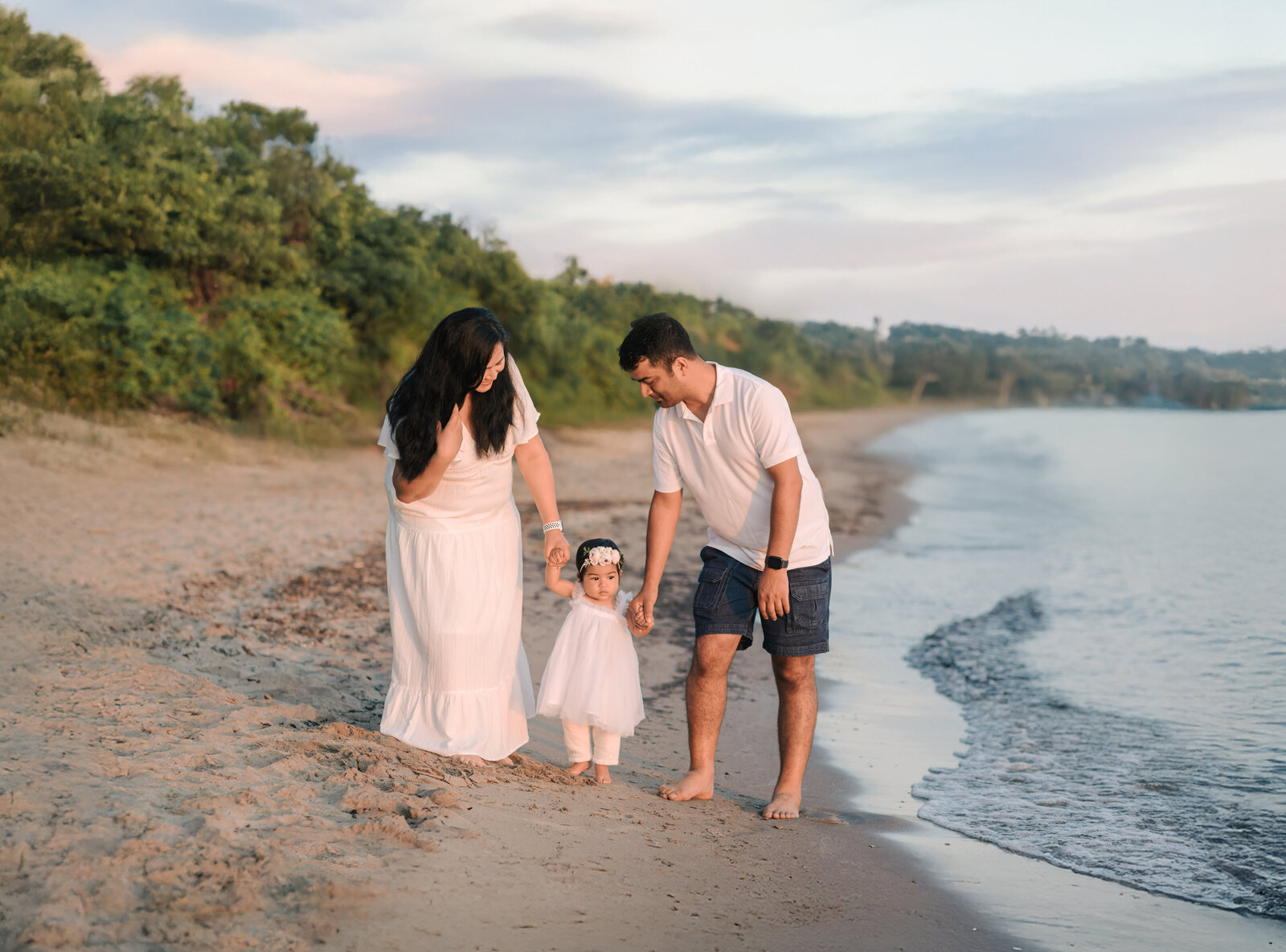 mom and dad holding daughters hand walking on beach