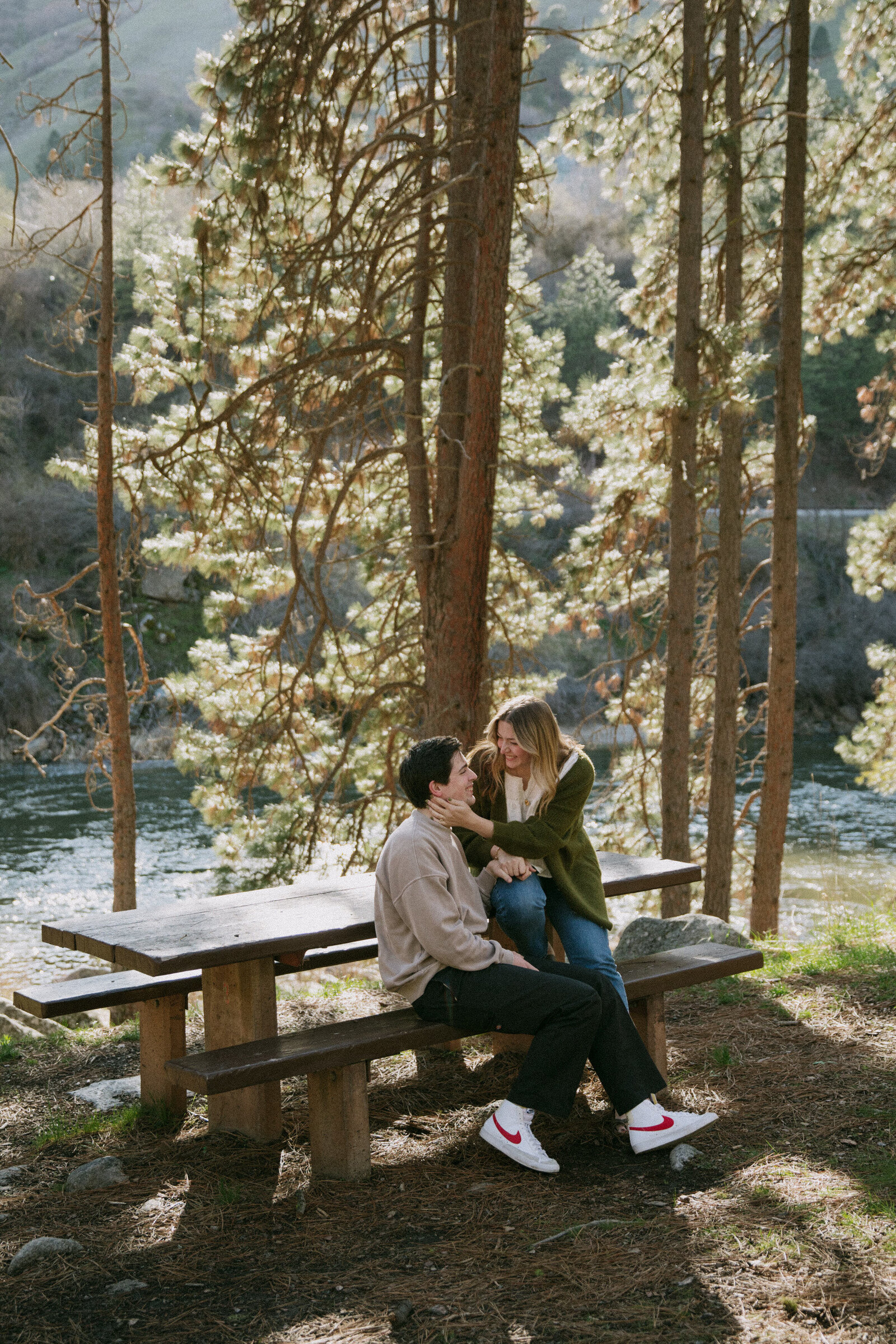 Couple laughing together on picnic table near California river during engagement session