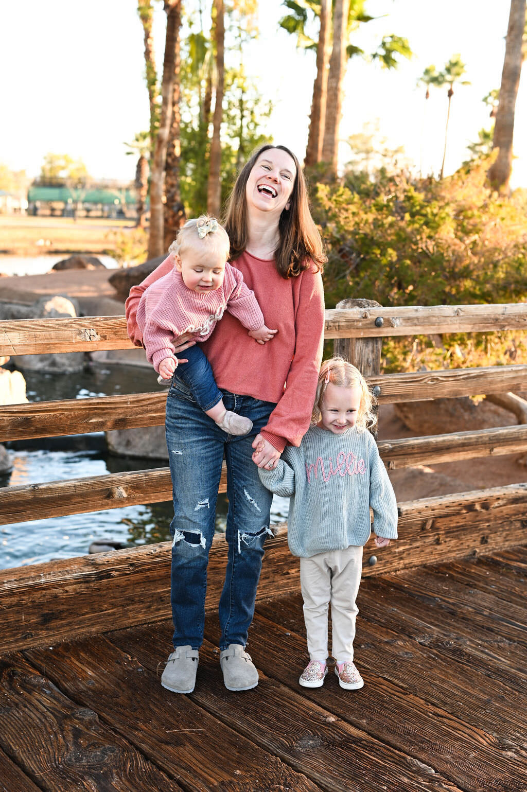 A mom standing on a bridge holding a small child on her hip as another stand beside her holding her hand.