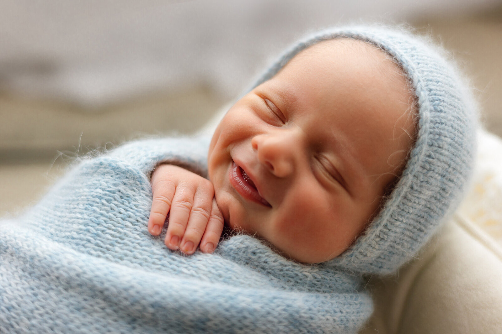 newborn baby boy wrapped in a blue swaddle with a bonnet smiling