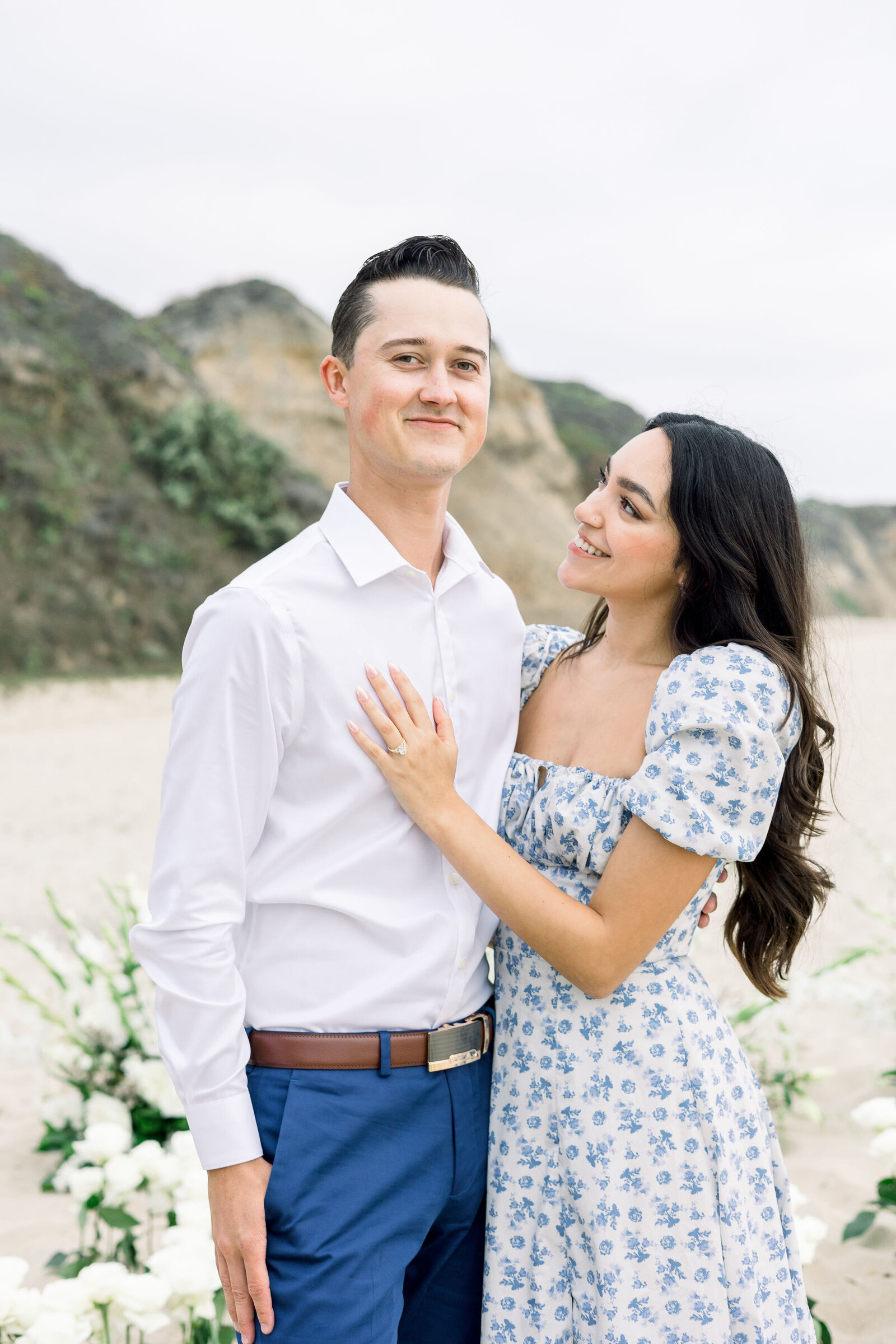 couples photography with man and woman standing together on the beach after a surprise proposal with florals behind them on the beach captured by wedding photographer bay area