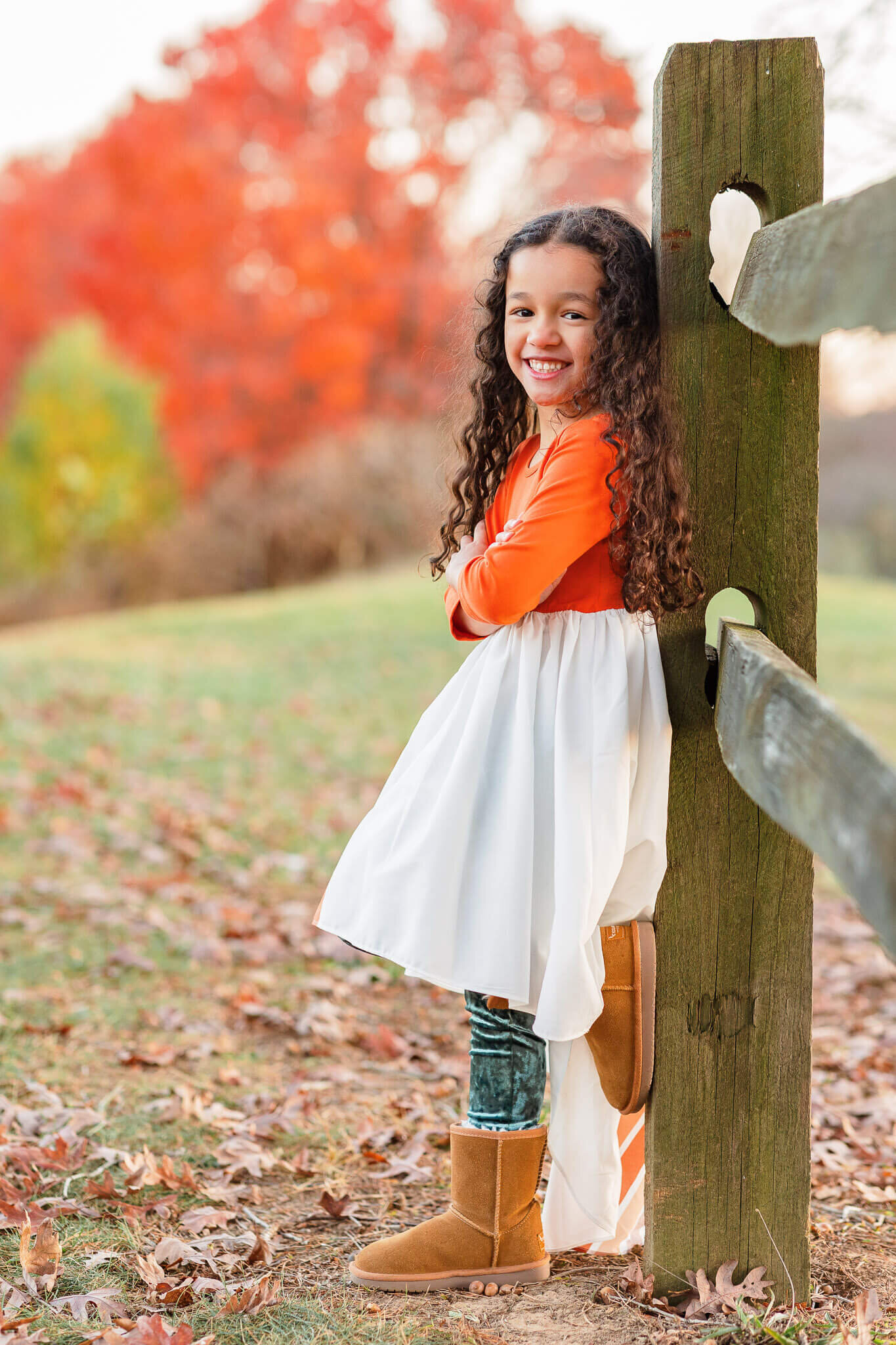 A little girl in a dress leaning up against a fence