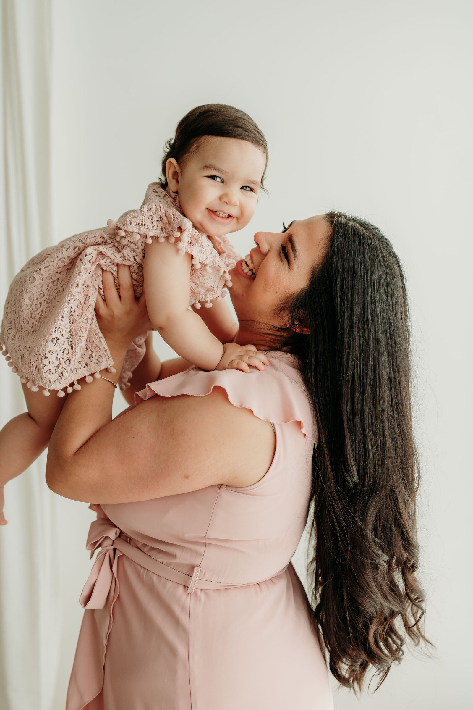 a mom holds her 1 year old baby and smiles at her during baby's first birthday session