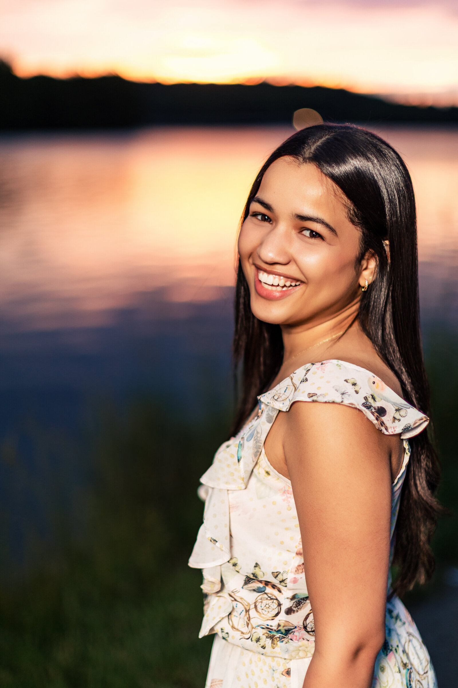 A dark hair smiling senior Post against the  Moraine State Park Lake at Sunset
