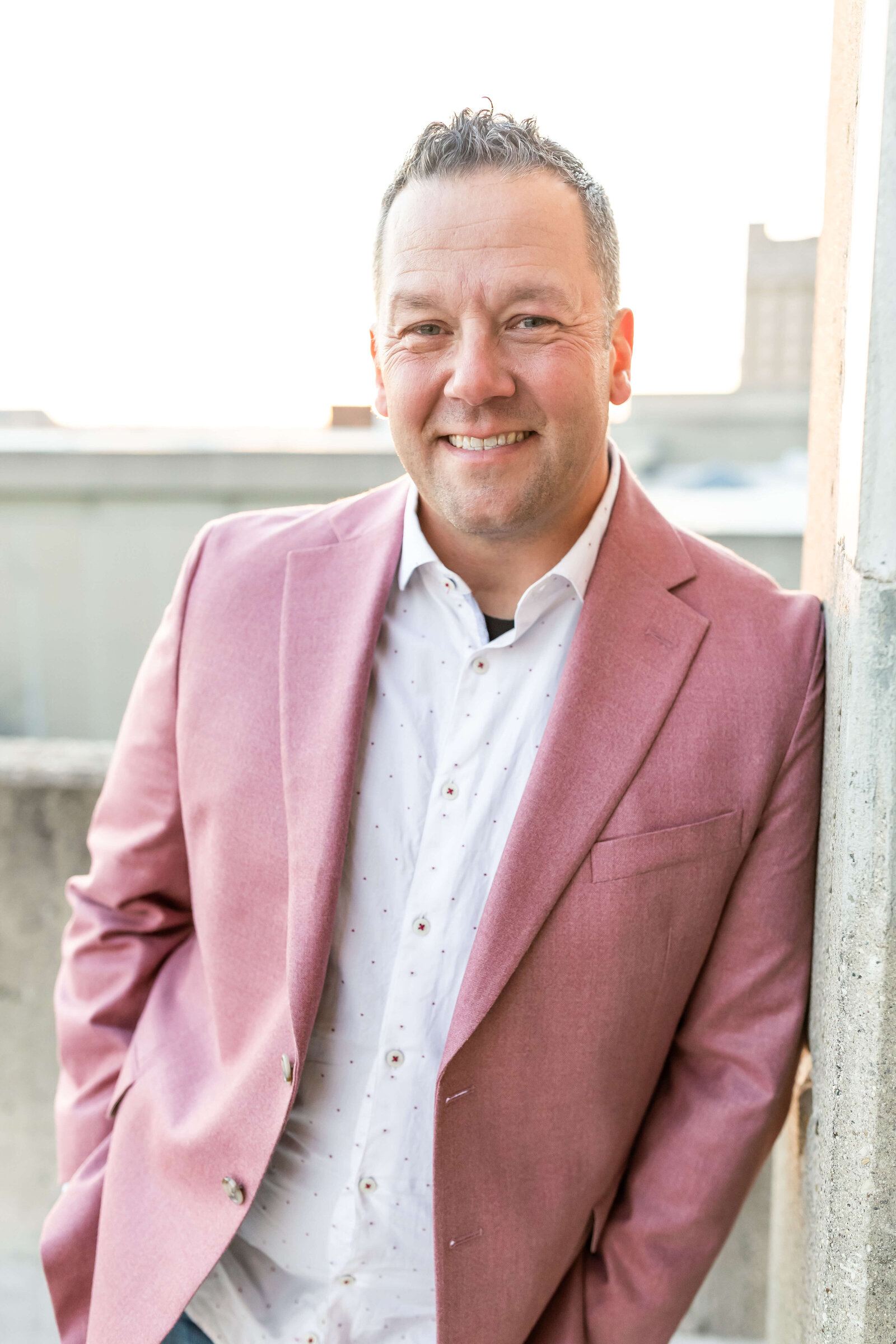 man smiling for camera for headshot wearing light red blazer and white button up