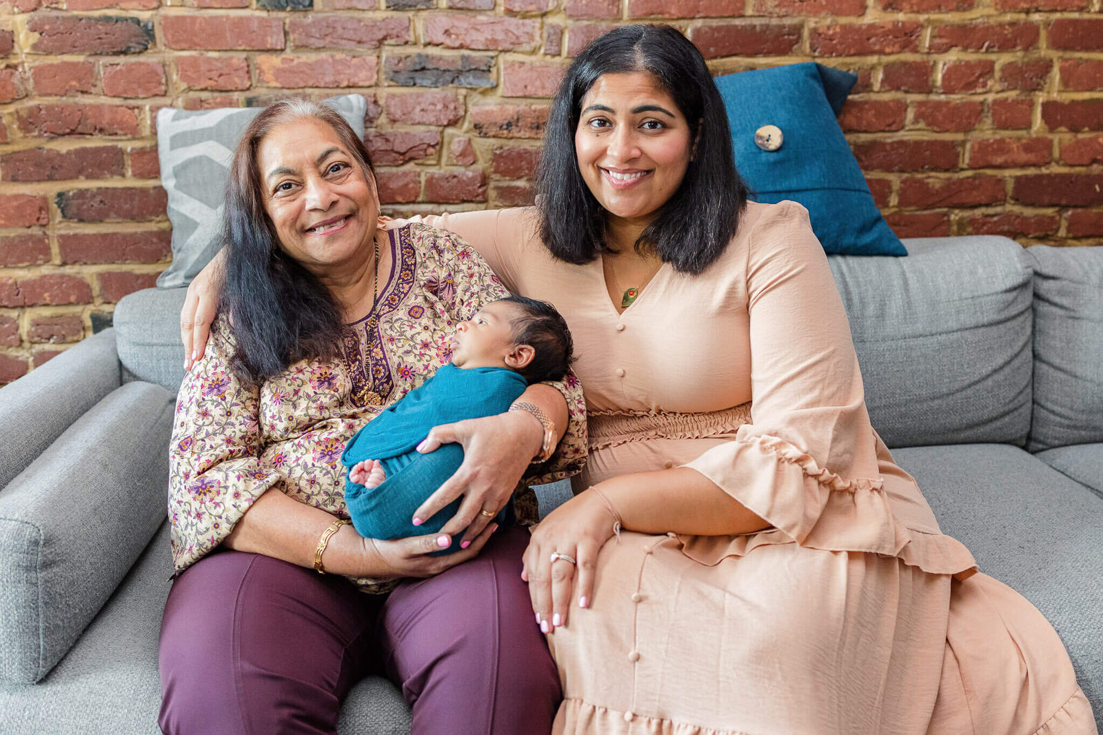 A grandma and mom sitting on the couch holding a newborn boy.