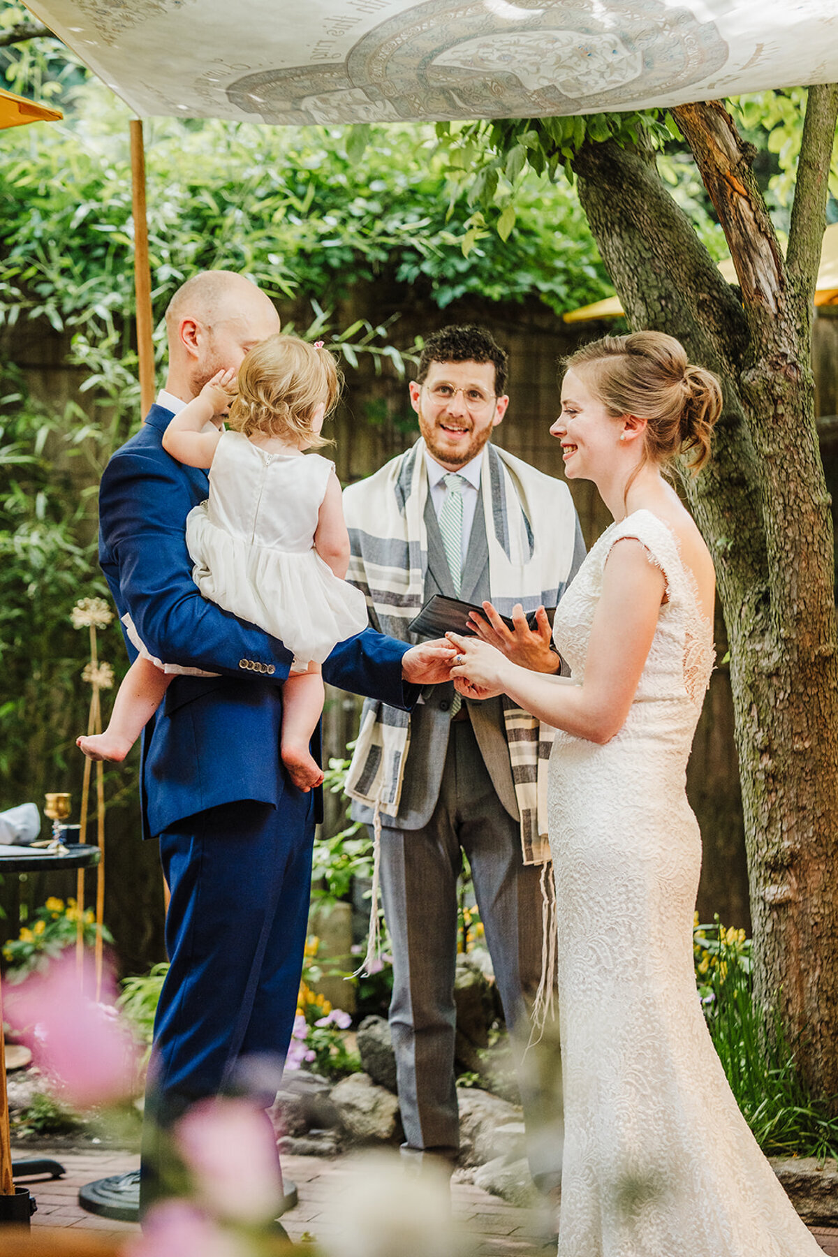 couple stands under chuppah with daughter as rabbi marries them