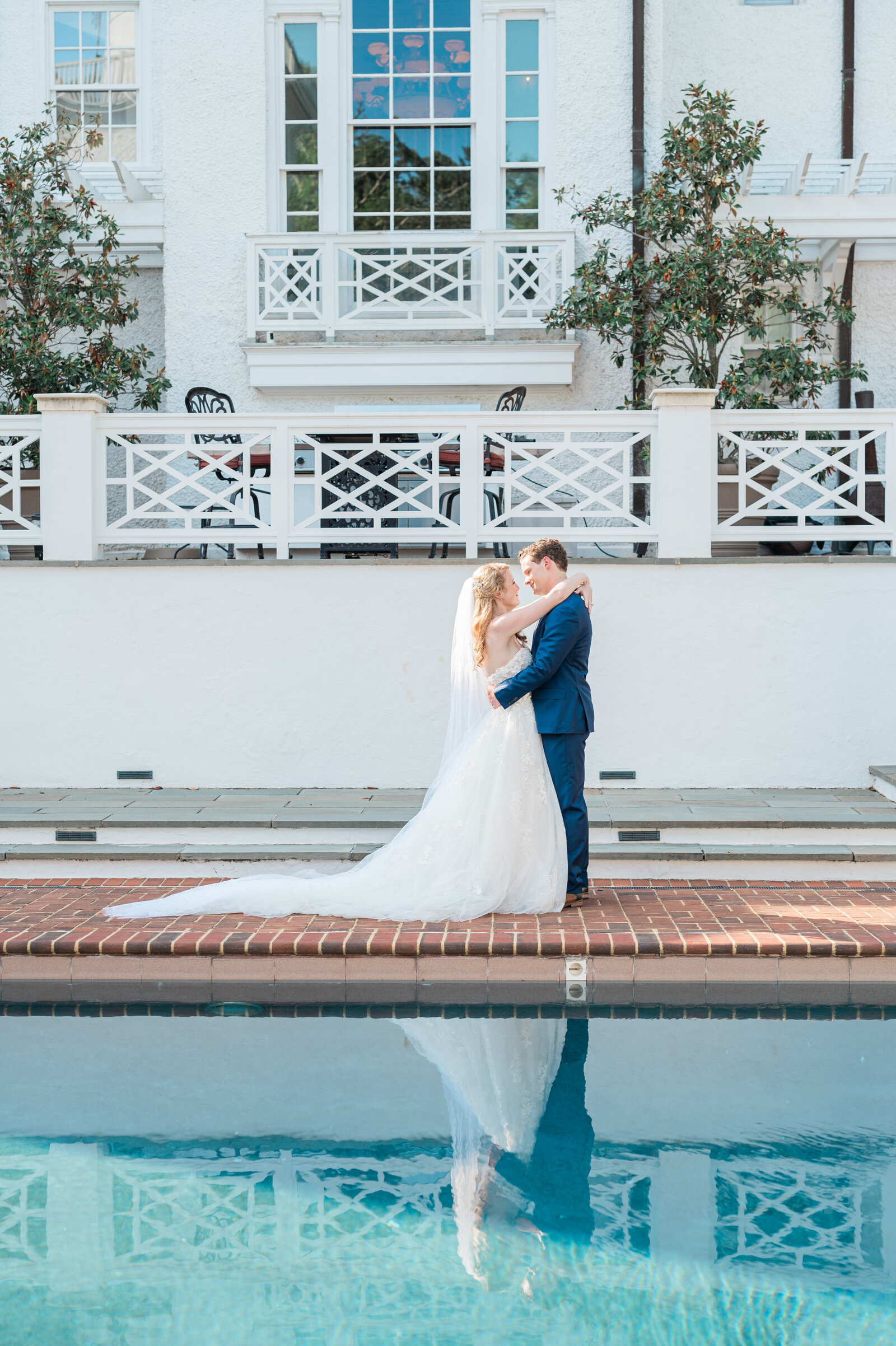A newlywed couple with their arms around each other at the edge of a pool