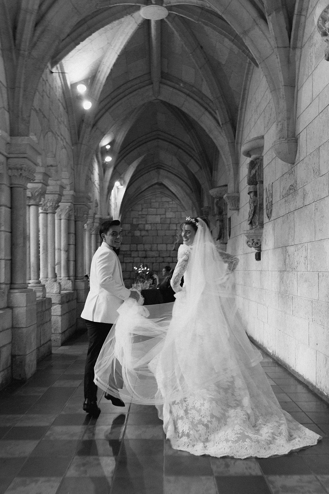 Bride and groom walking down the hallway of a historical wedding venue in black and white | Sush Digital Media