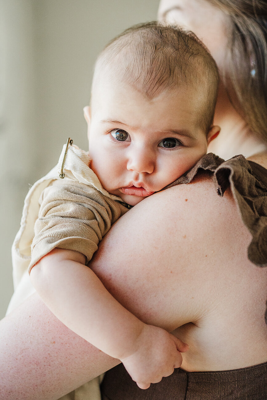 baby stares into camera over mothers shoulder