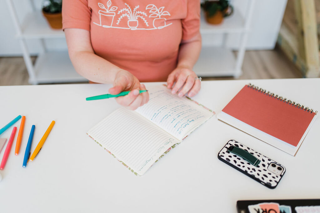 Copywriter Sara Gillis writing in a notebook at a desk