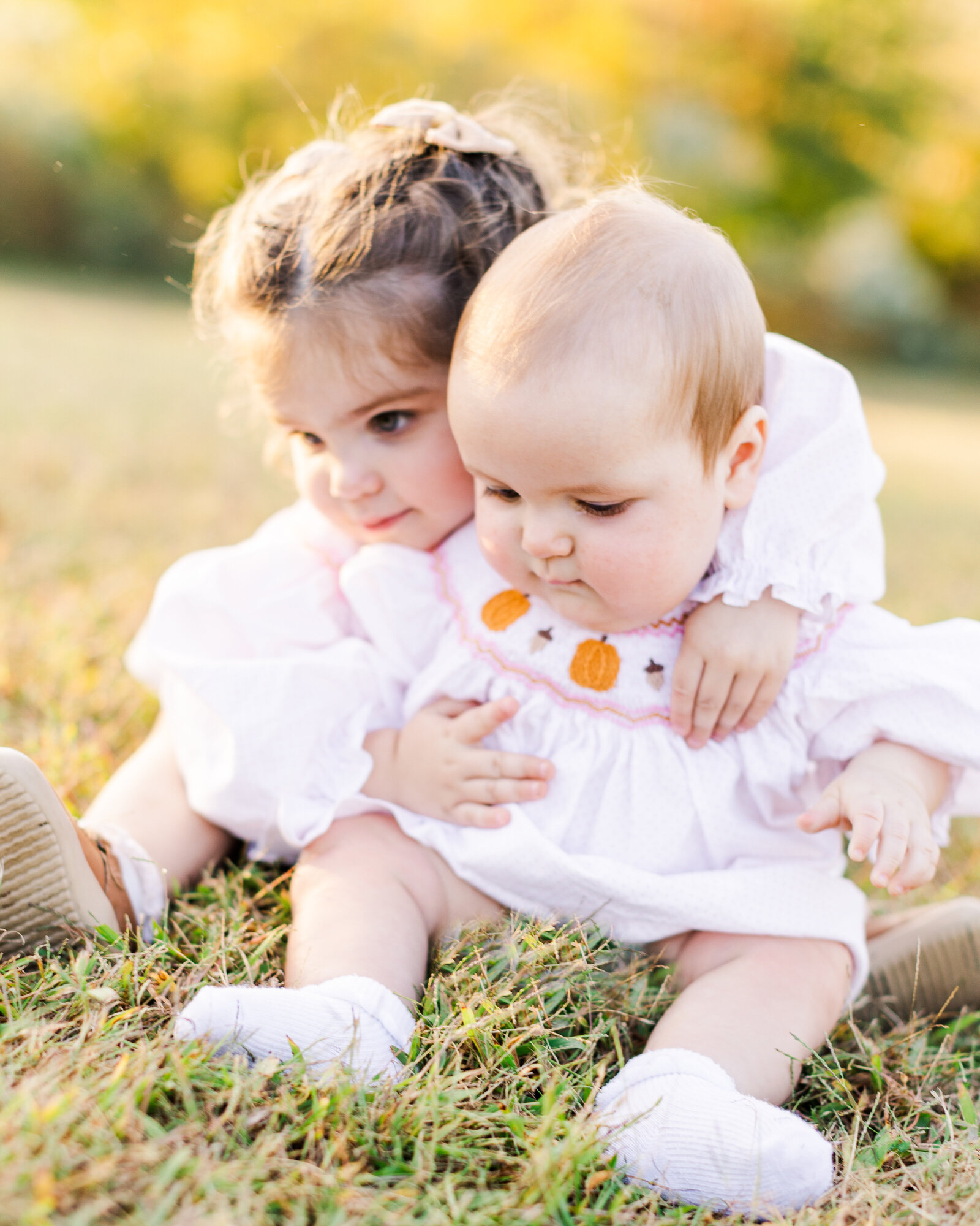 Savannah Taunton’s two daughters sitting on the grass in matching smocked dresses, captured by Abby Bell Photography, Fine Art Portrait Photographer based in Alabama.