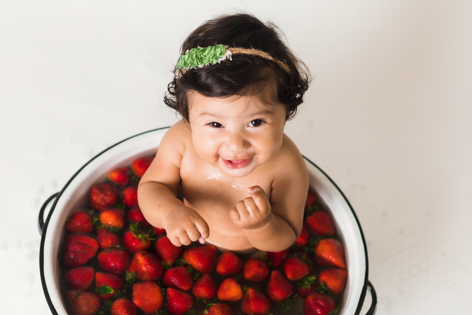 Milestone Photographer, a baby girl sits in a ceramic pot filled with floating strawberries
