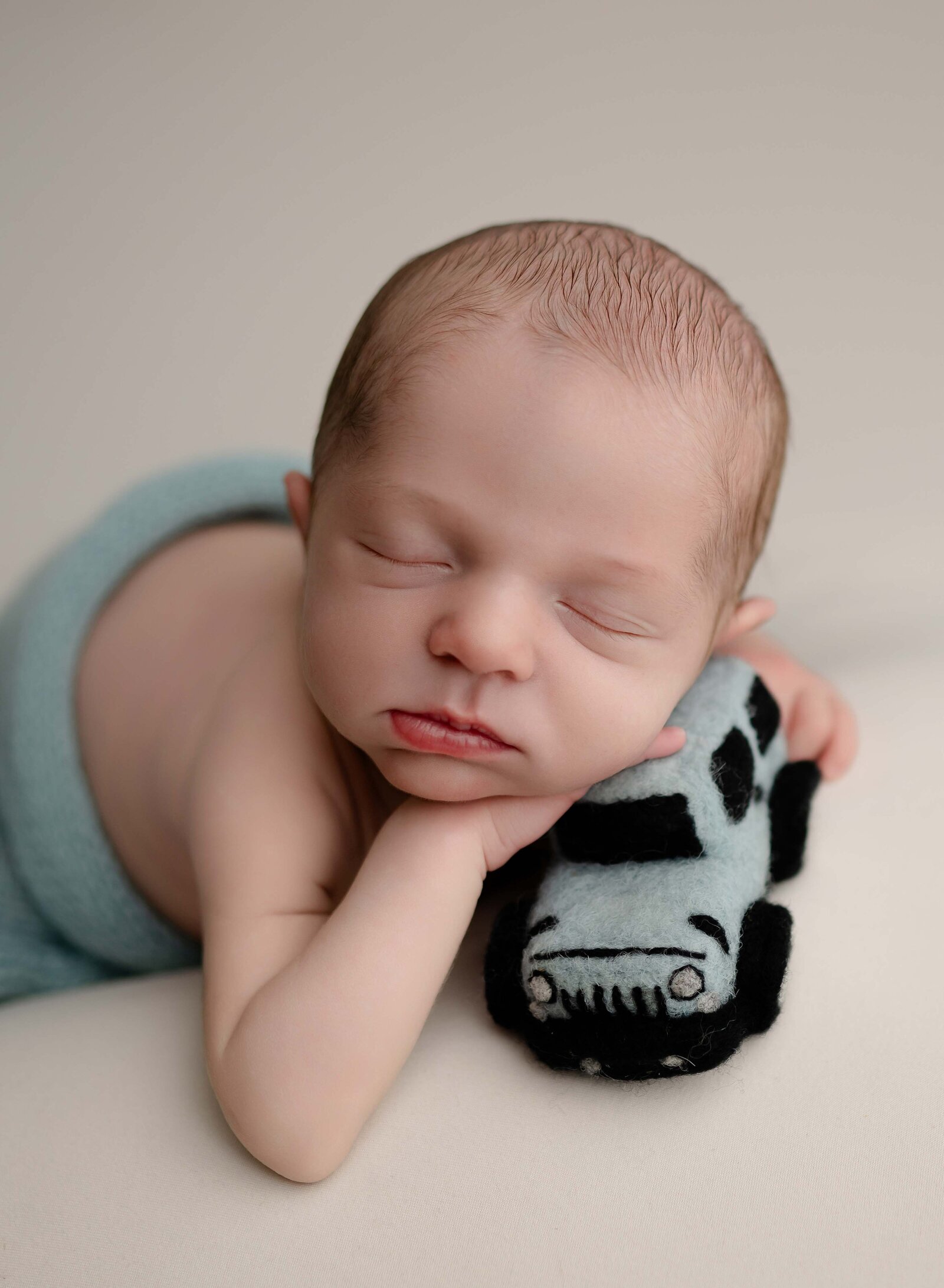 Baby sleeping on tummy and holding a blue felted jeep prop. Photo taken by Jenni Nikki at Newborn photo studio in Atlanta, GA.