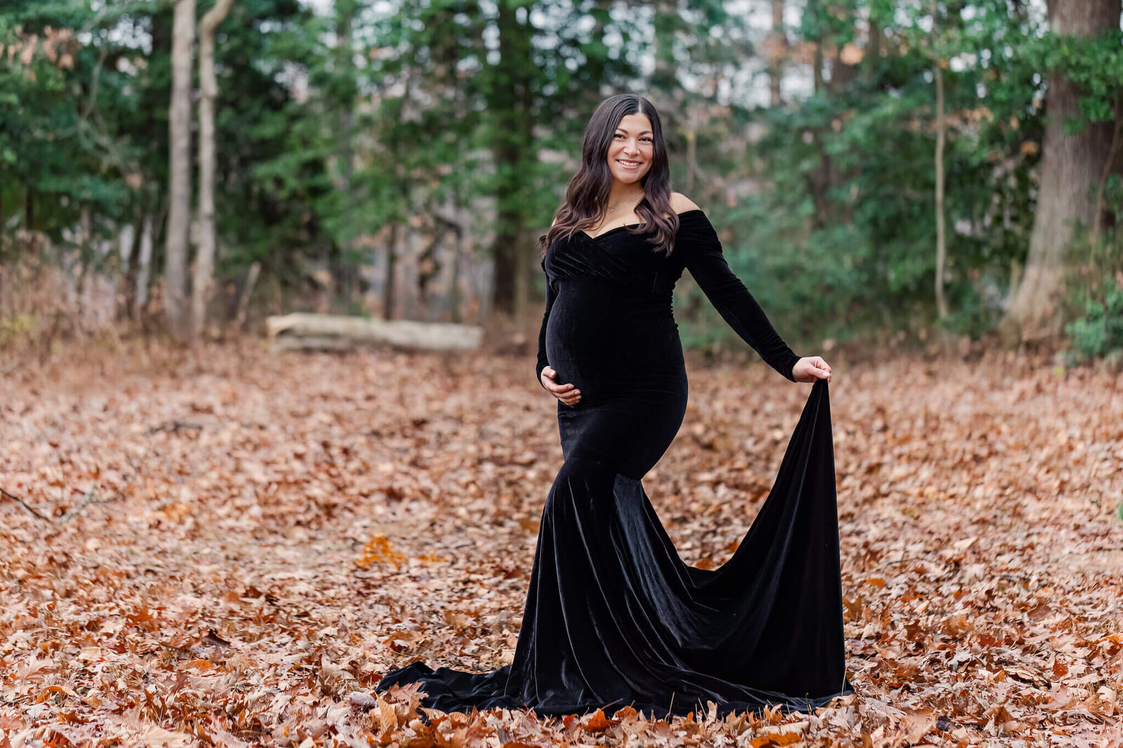 A momma-to-be holding her black dress behind her during her maternity portraits.