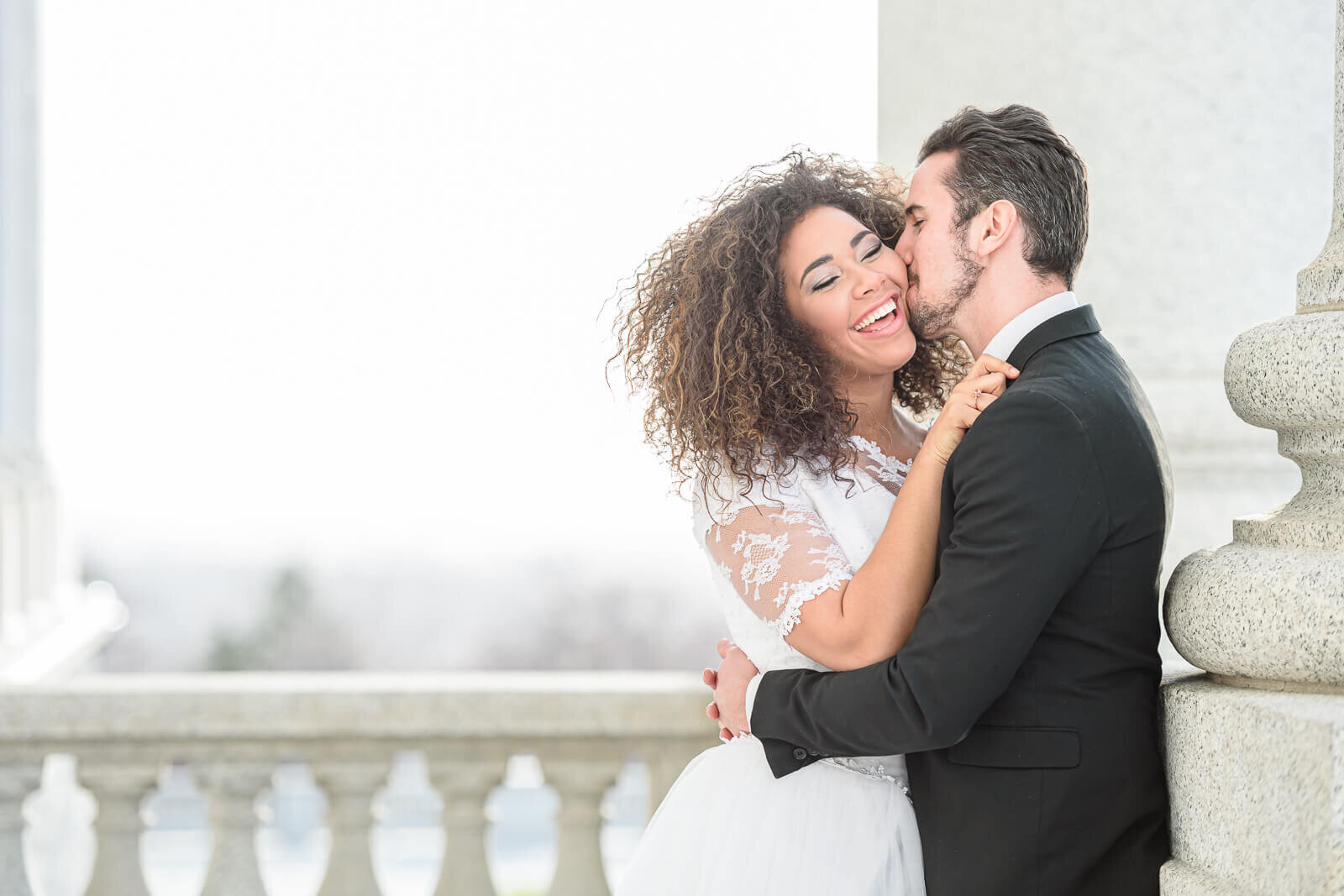 A groom kisses his bride on her cheek and holds her outside of the Utah State Capitol building