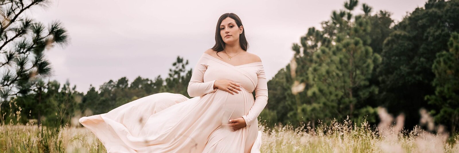 pregnant woman in cream dress standing in a field of wildflowers with her dress blowing in the wind near Orlando, FL