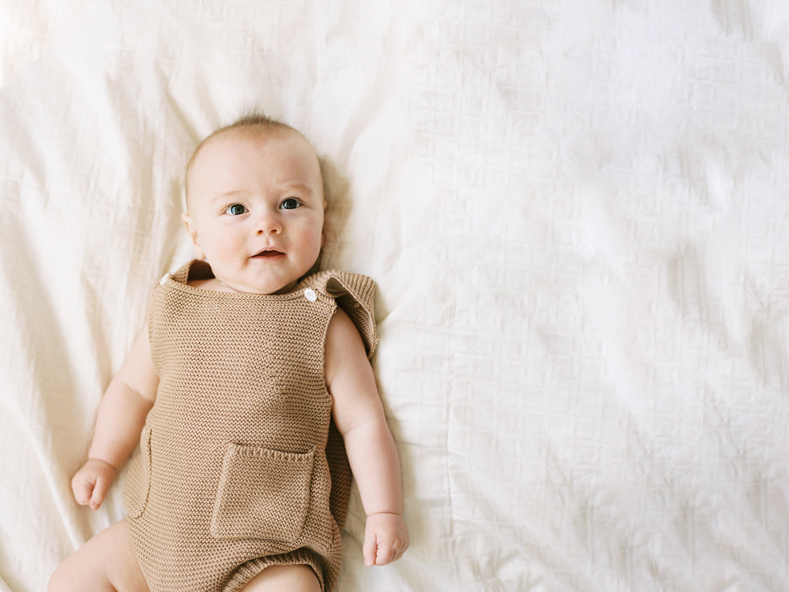 6 month old laying on a bed in knit overalls